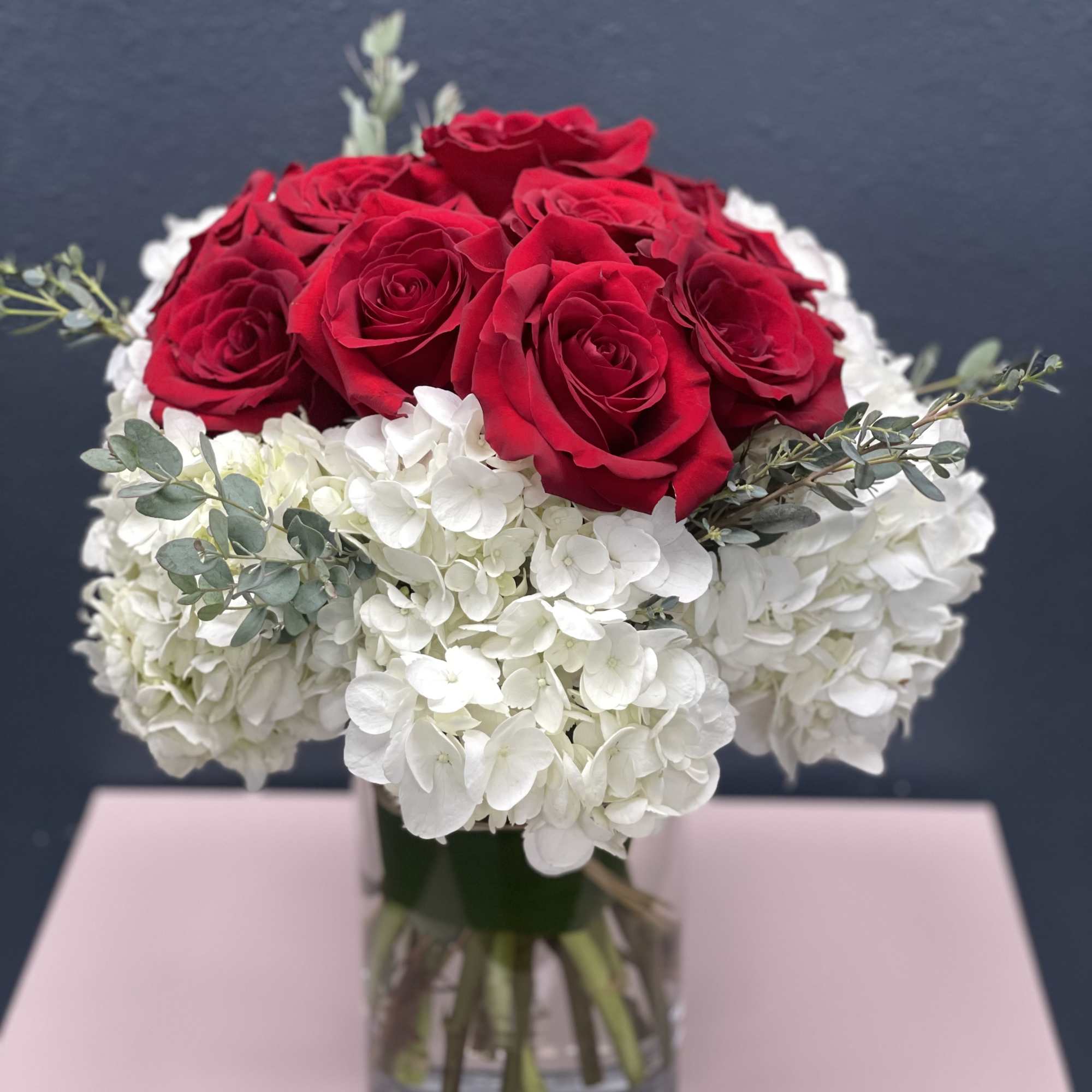 Red roses arranged with white hydrangeas in a glass vase