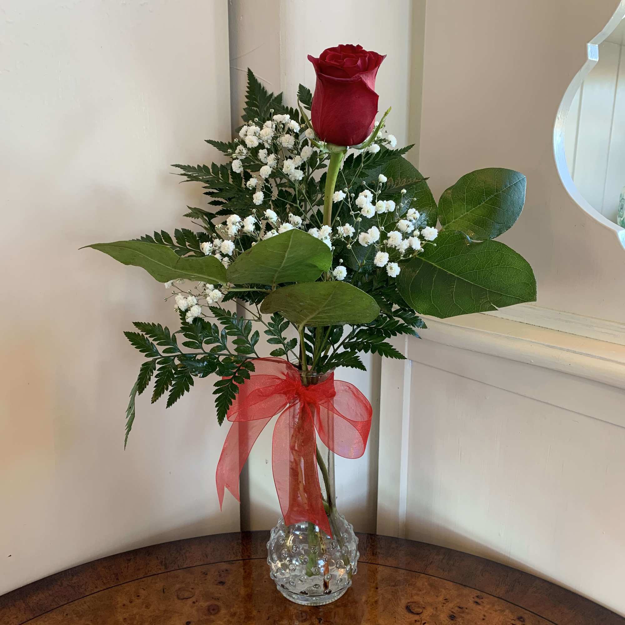 Single red rose in a clear vase with baby's breath and a red ribbon