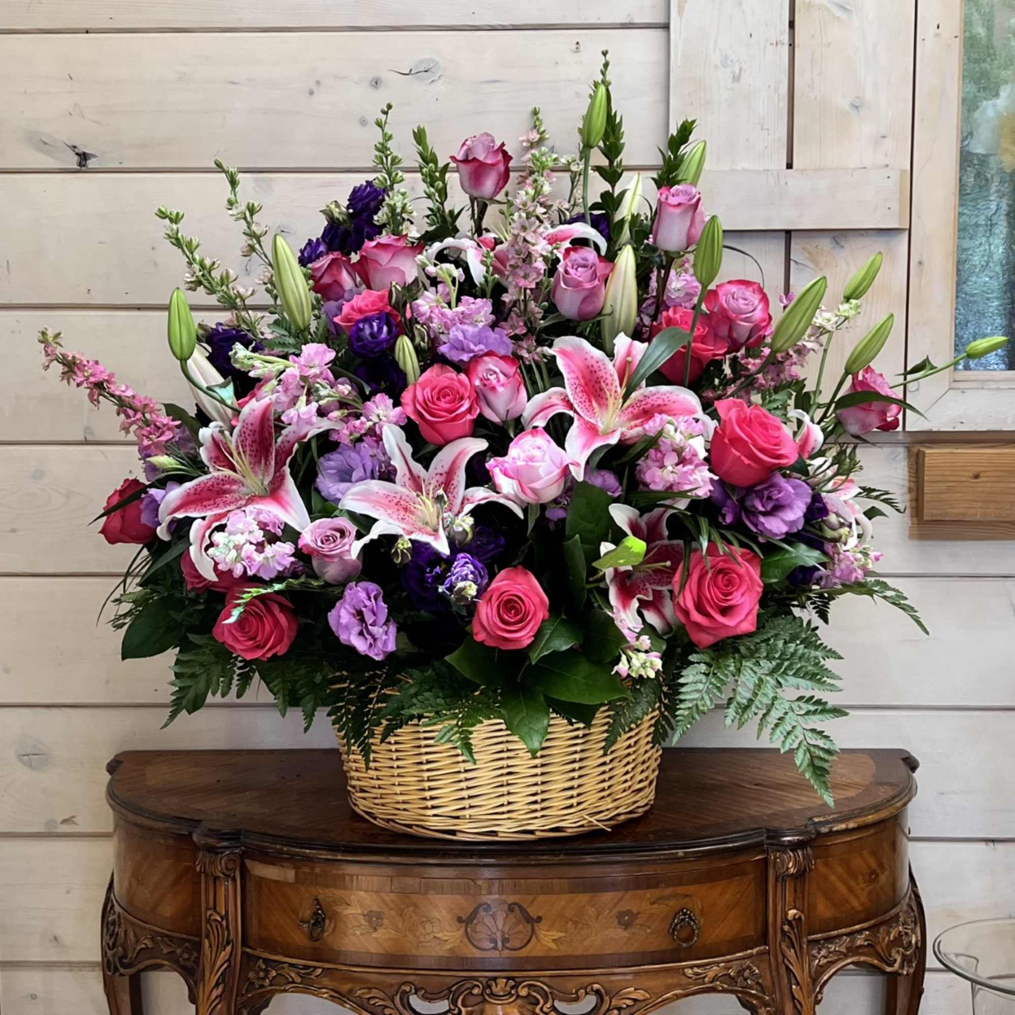 Basket arrangement of pink roses, lilies, and purple flowers