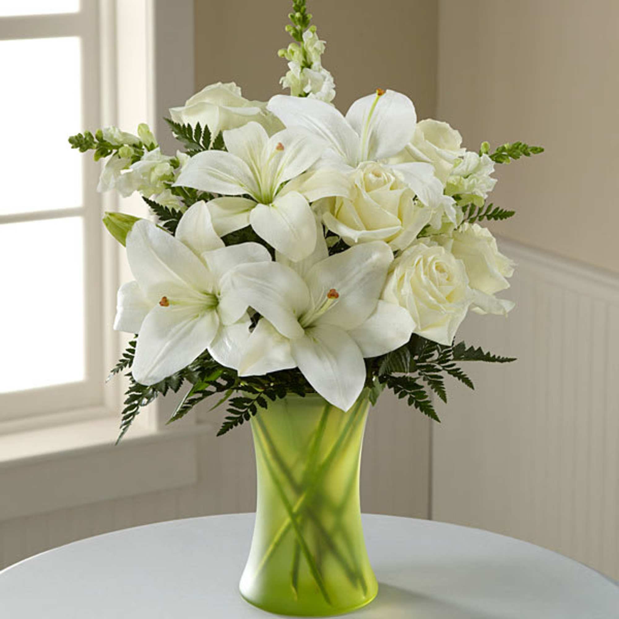 White lilies and roses arranged in a green glass vase