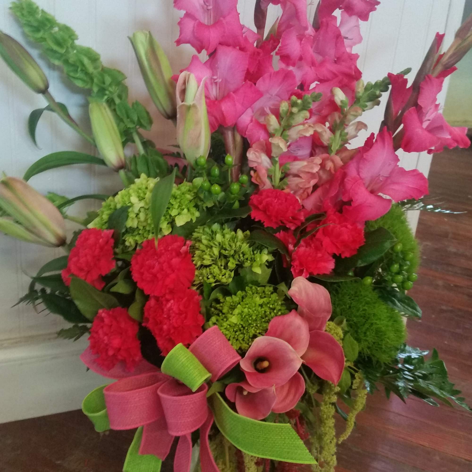 Pink gladiolus and calla lilies with red carnations in a ribboned bouquet
