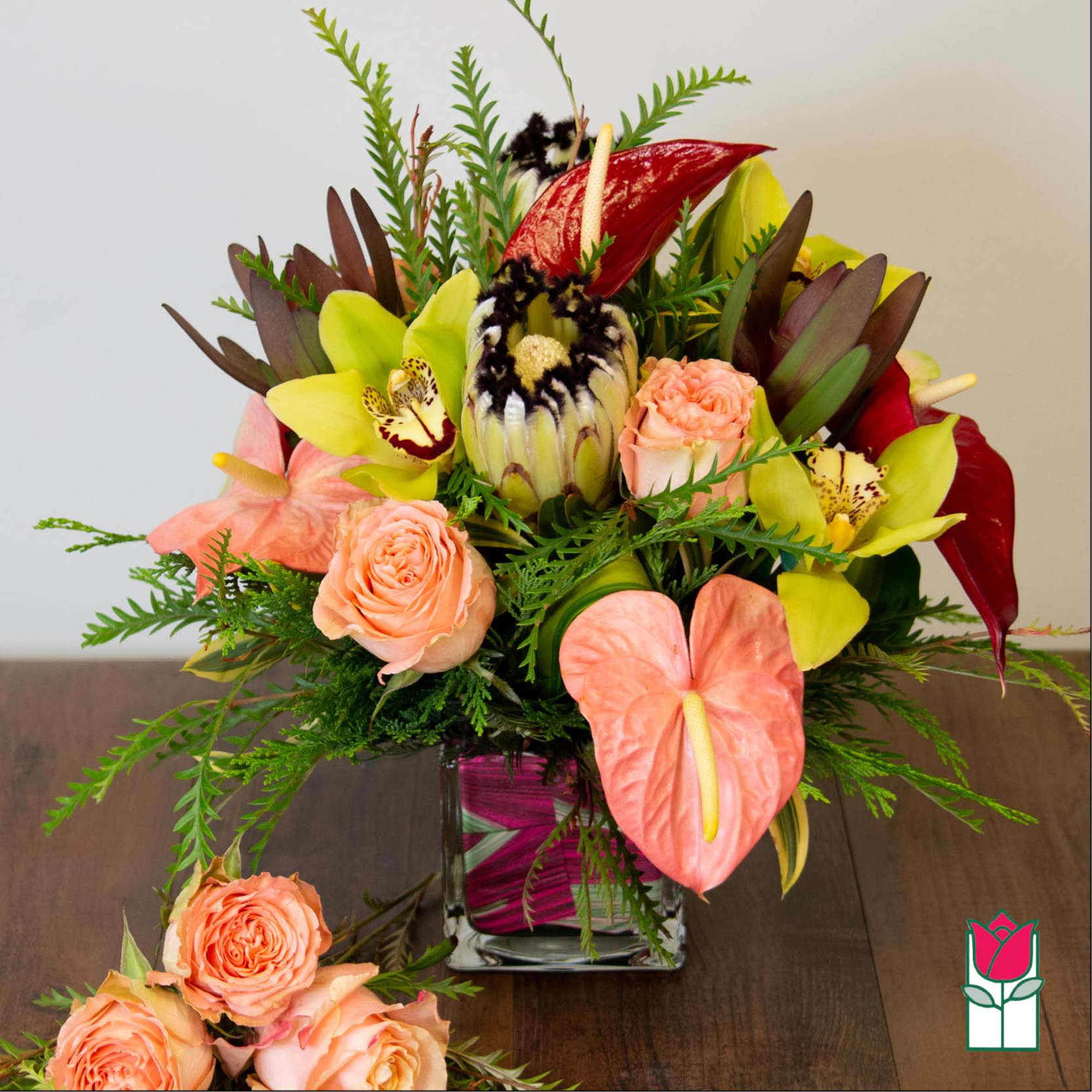 Tropical bouquet with peach roses, anthuriums, and yellow orchids in a glass vase