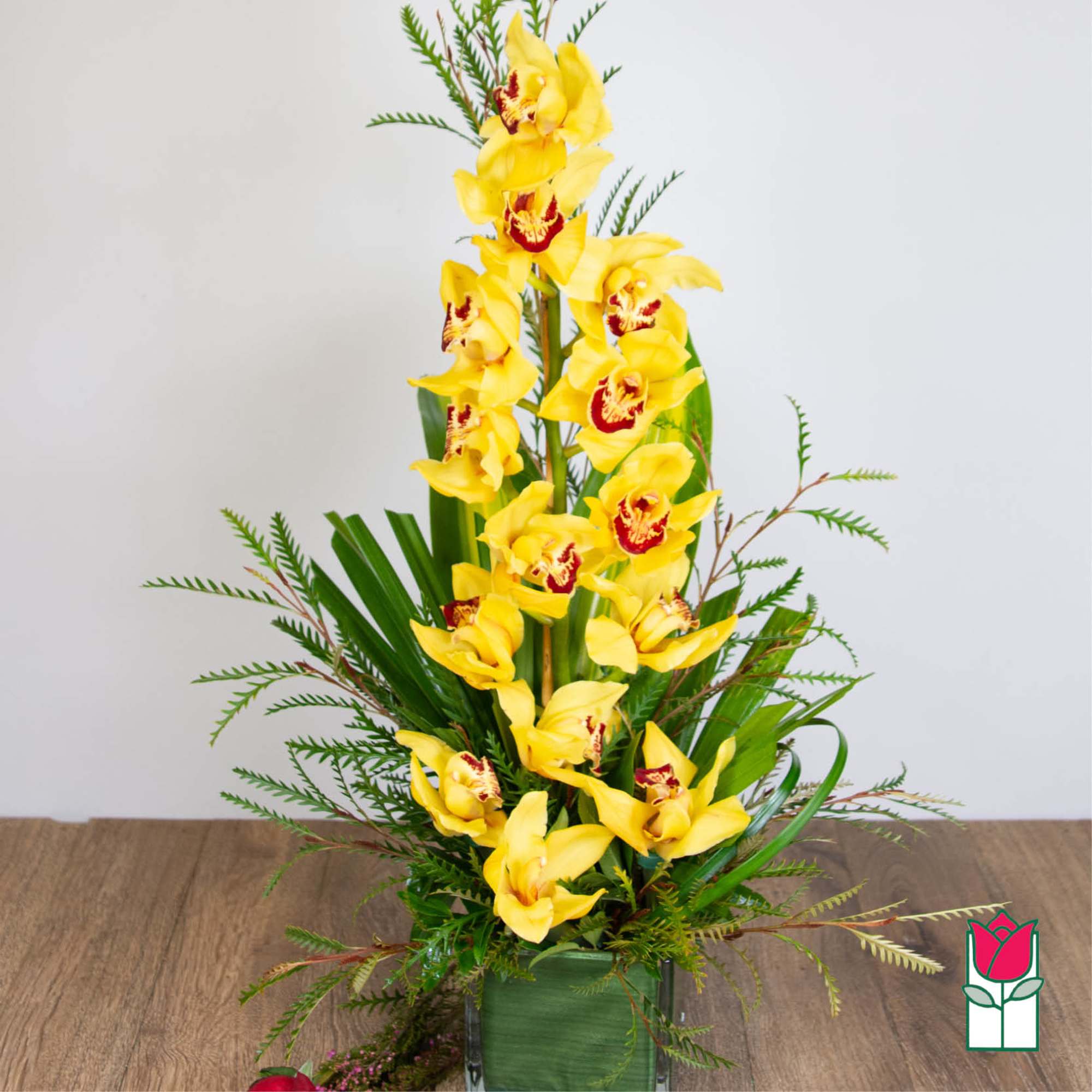 Tall arrangement of yellow cymbidium orchids in a square glass vase with linear foliage