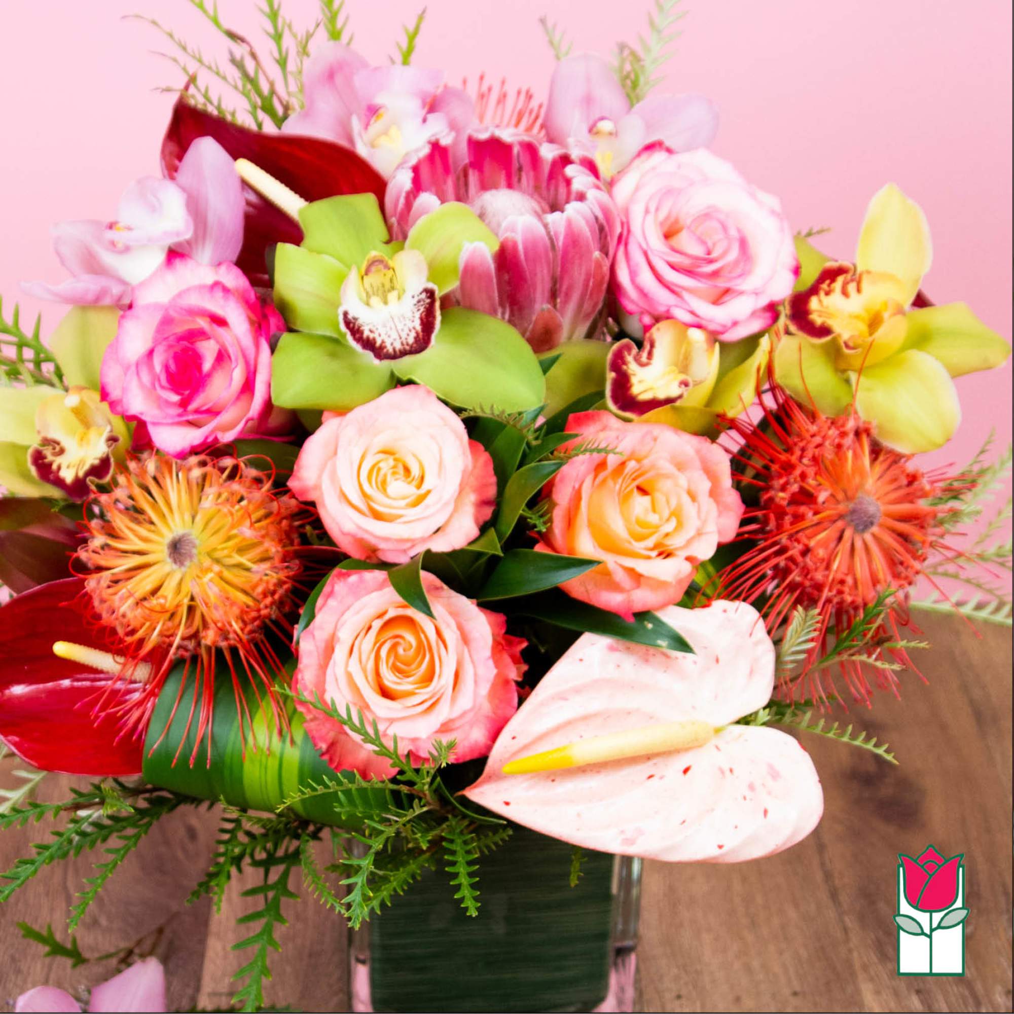Mixed bouquet of pink roses, orchids, and anthuriums in a glass vase