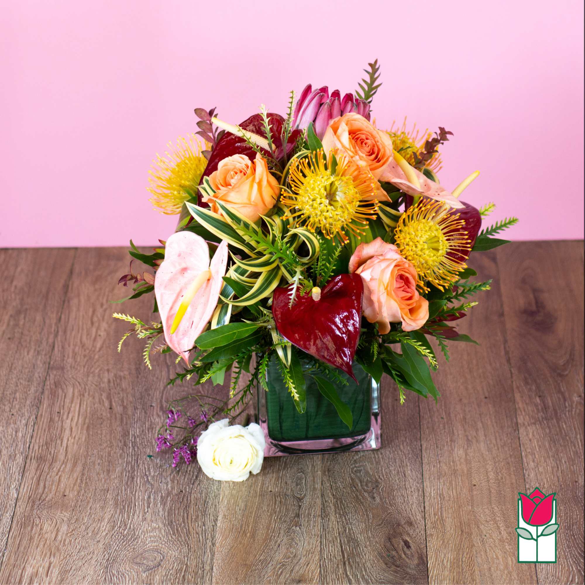 Mixed bouquet of peach roses, pink anthuriums, and yellow pincushion blooms in a glass vase.