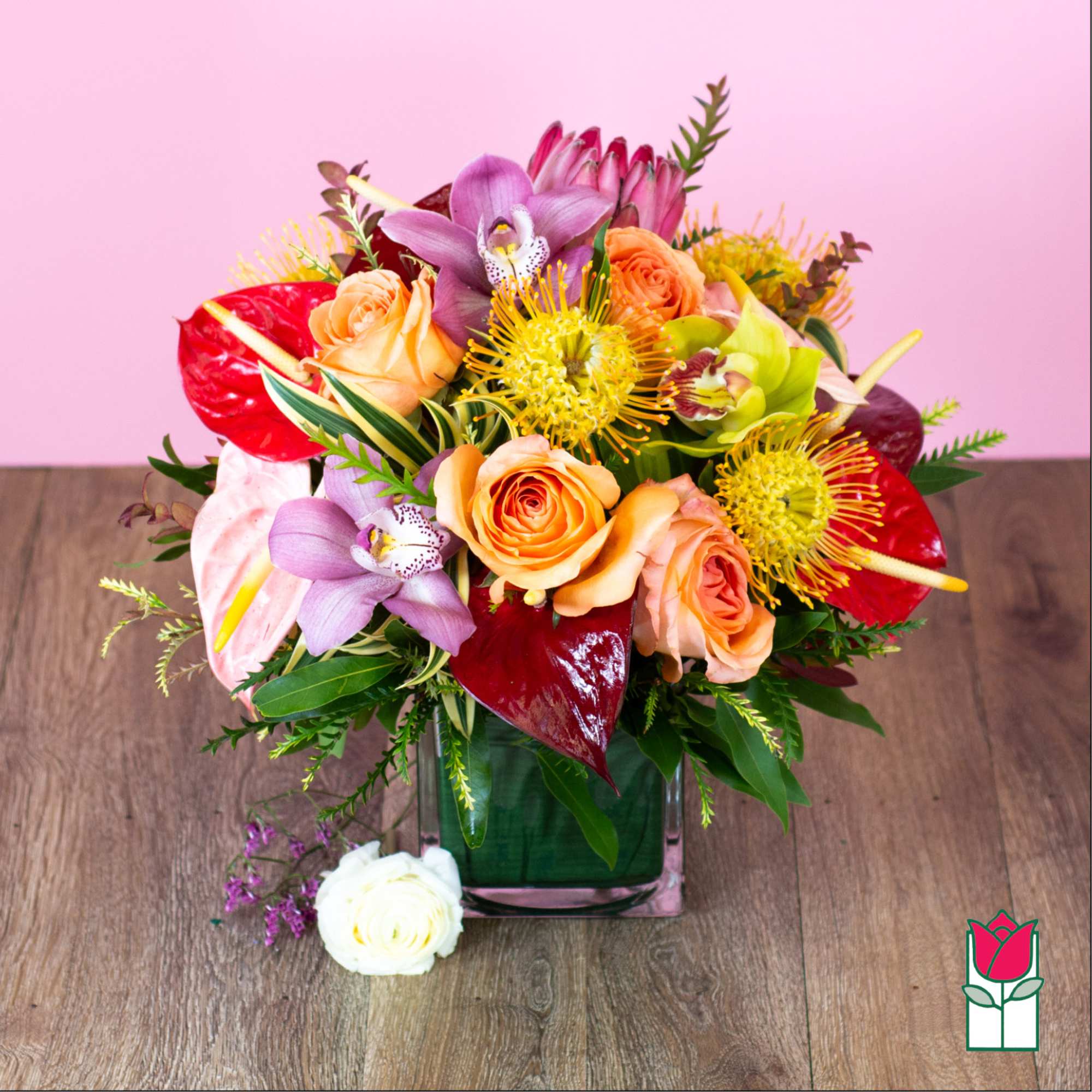 Colorful bouquet of roses, orchids, and tropical blooms in a square glass vase