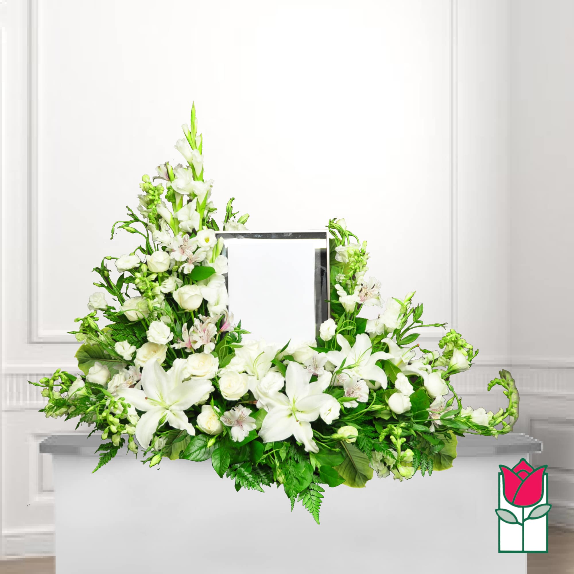 White floral funeral spray with lilies and roses around a framed photo
