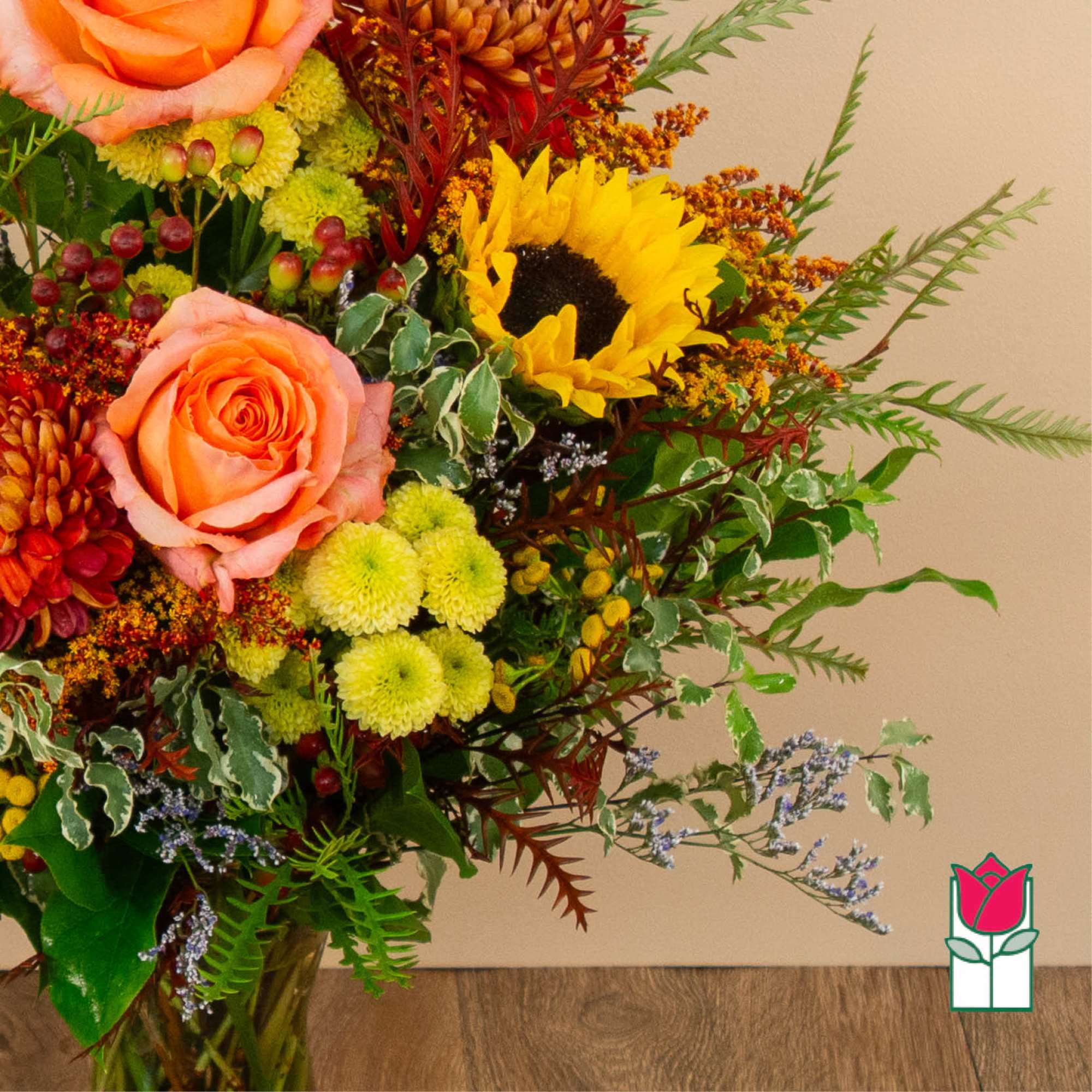 Mixed bouquet with peach roses, a sunflower, and yellow mums in a vase