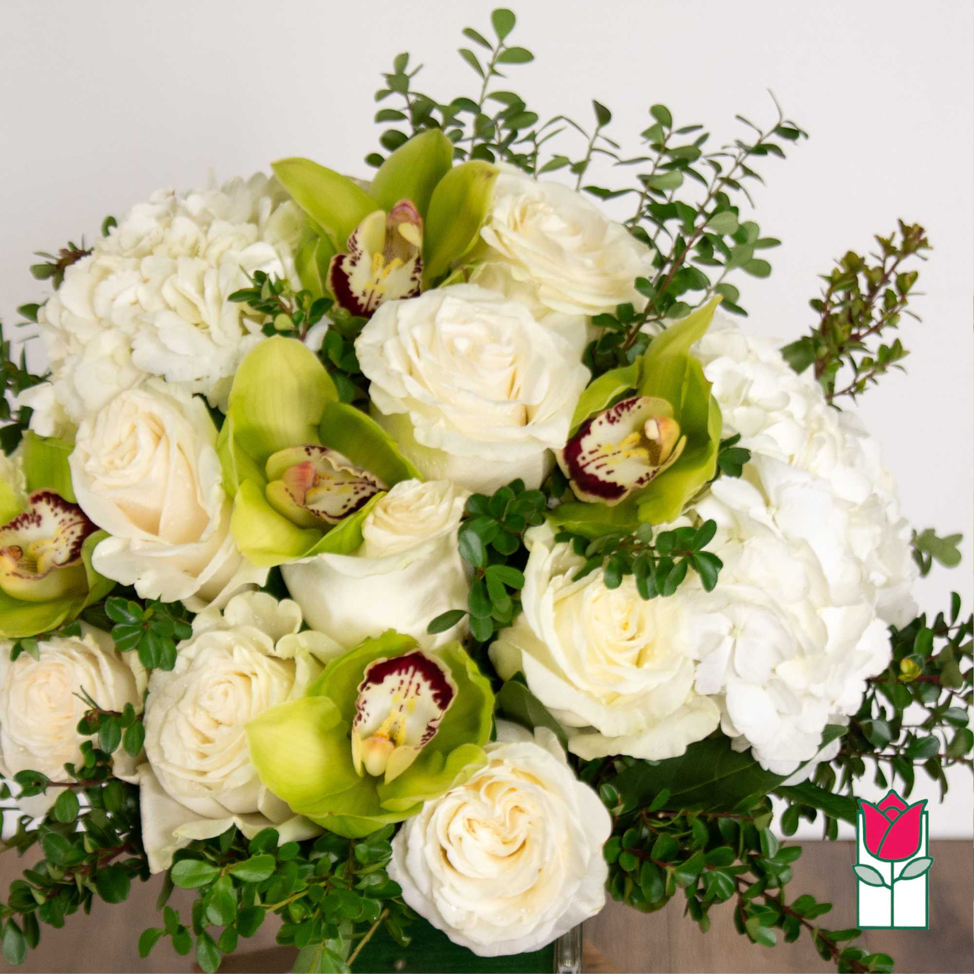 White roses and green orchids arranged with white hydrangeas in a vase
