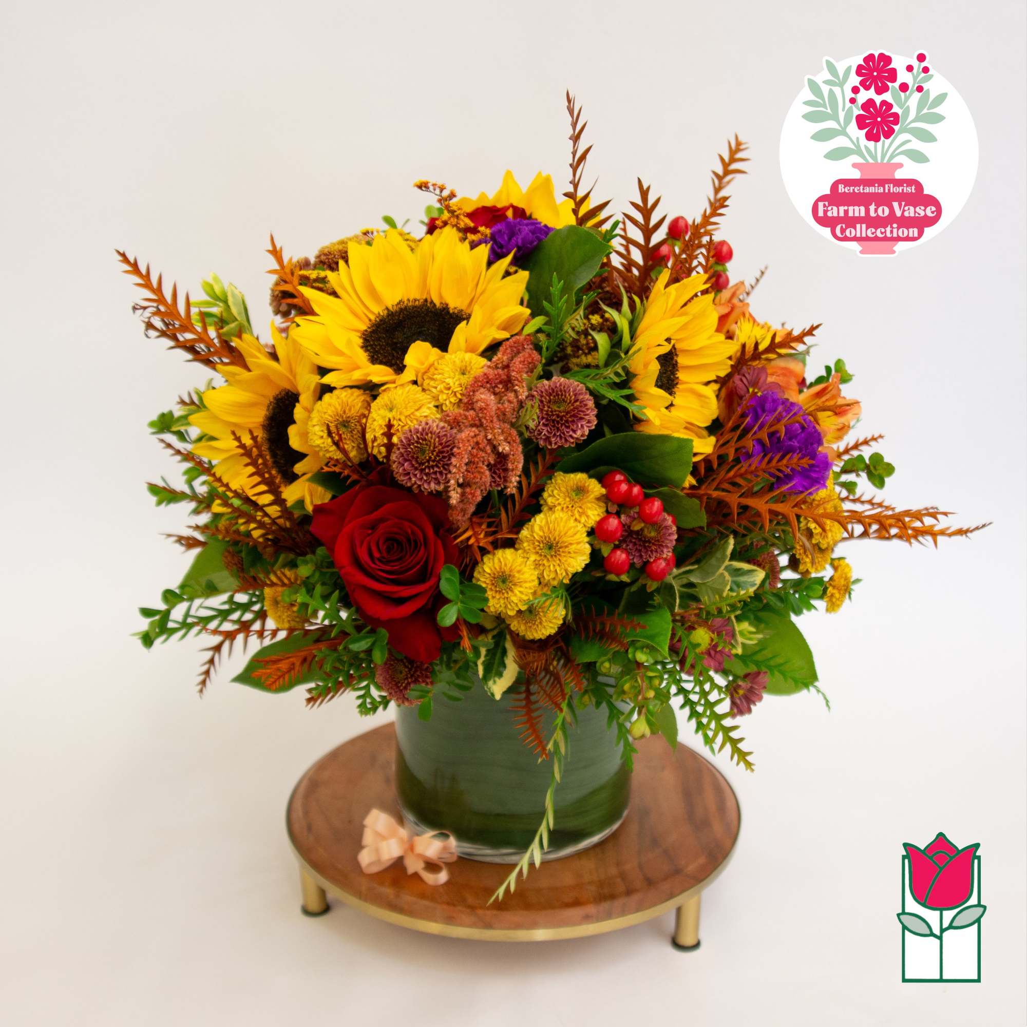 Mixed bouquet with sunflowers, a red rose, and yellow blooms in a green vase.