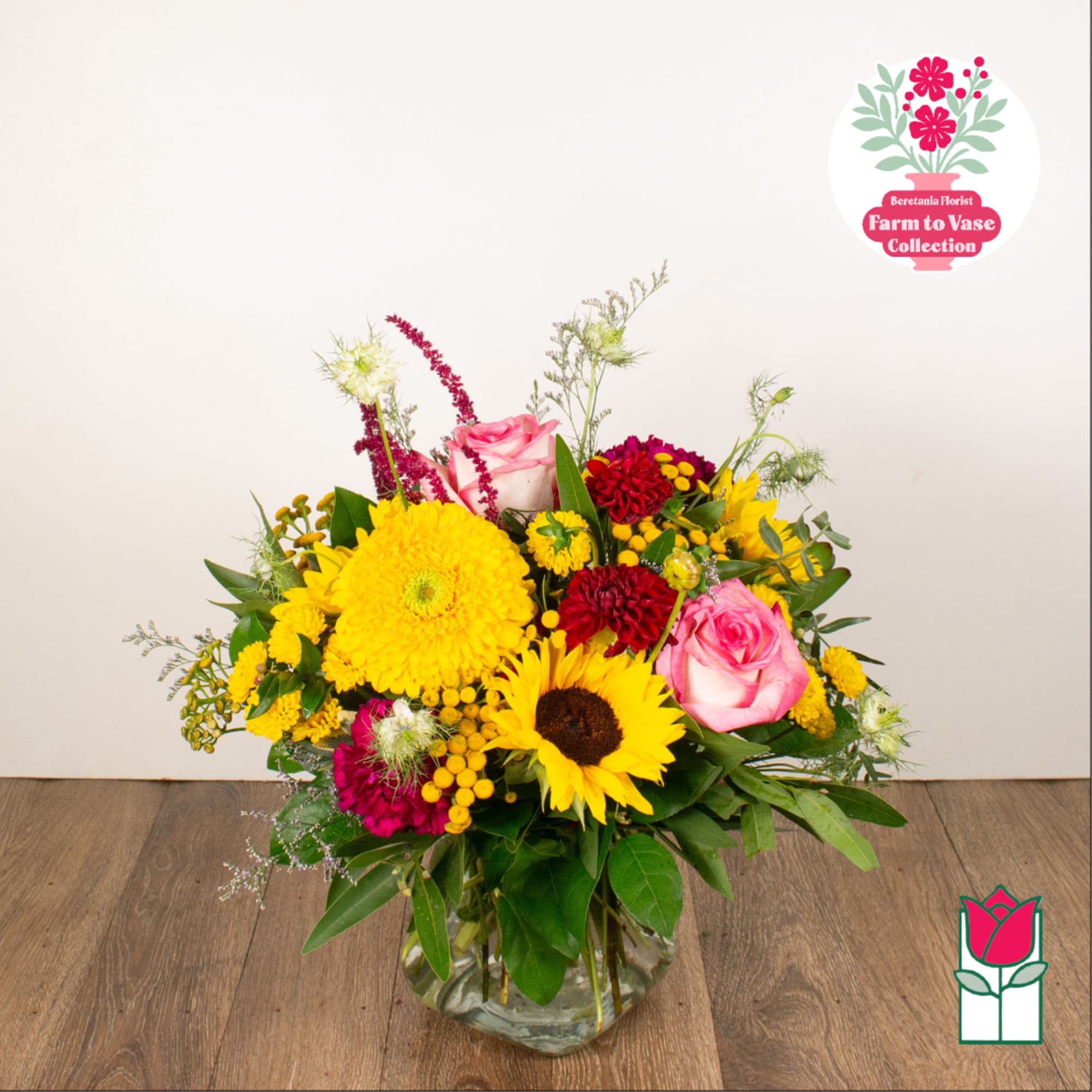 Mixed bouquet of pink roses, yellow sunflowers, and red blooms in a glass vase