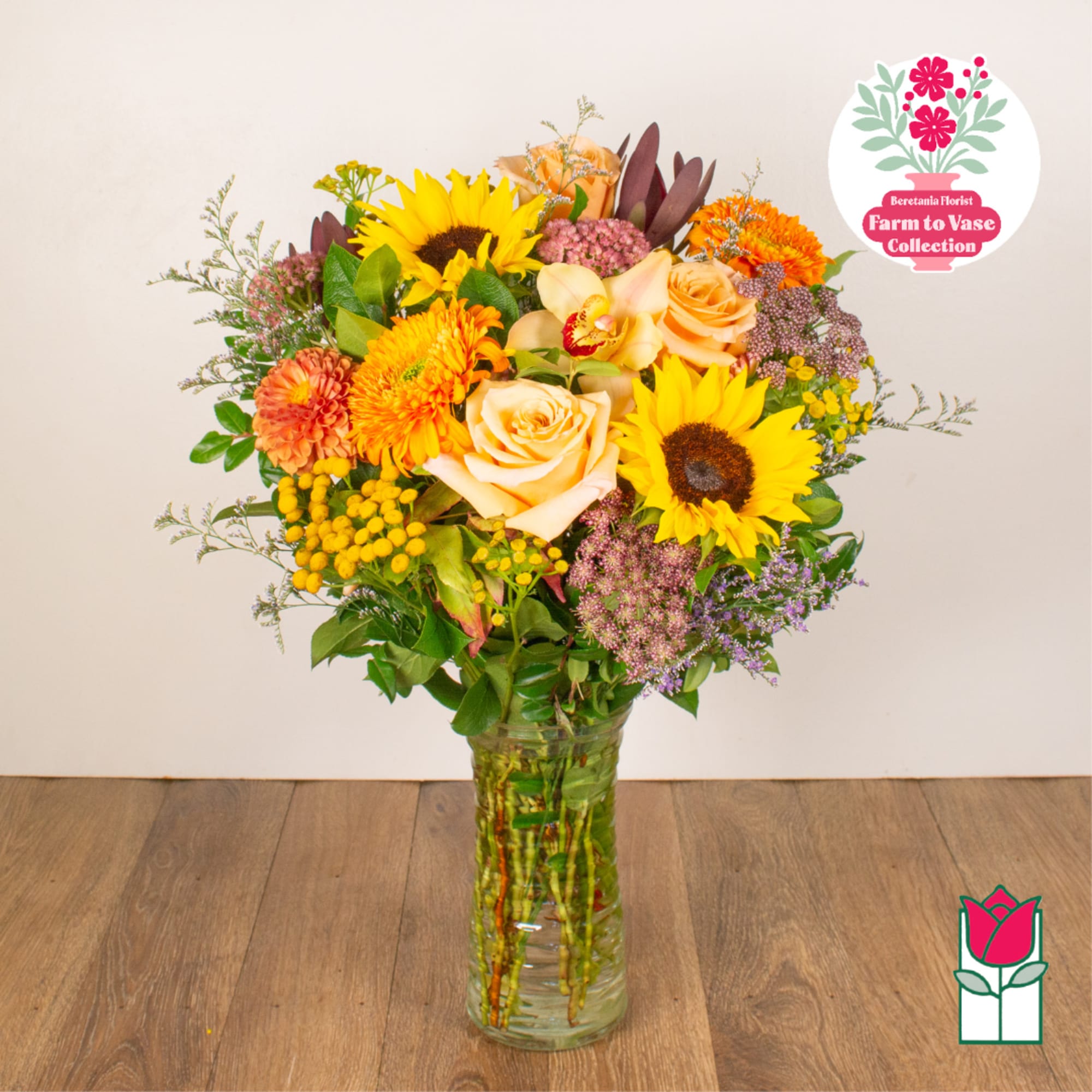 Mixed bouquet of sunflowers, roses, and mums in a glass vase