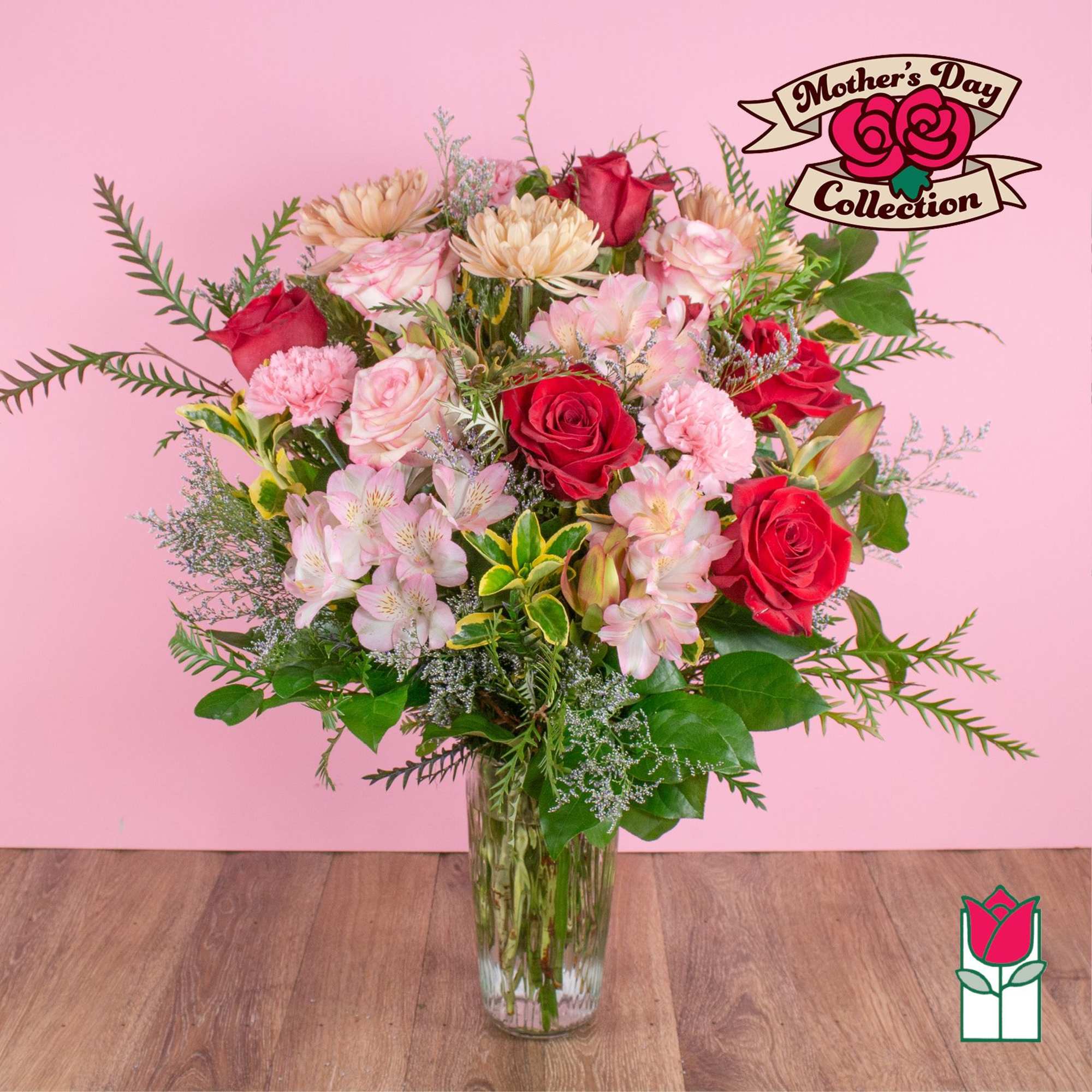 Tall mixed bouquet of red roses and pink flowers in a clear glass vase against a pink background