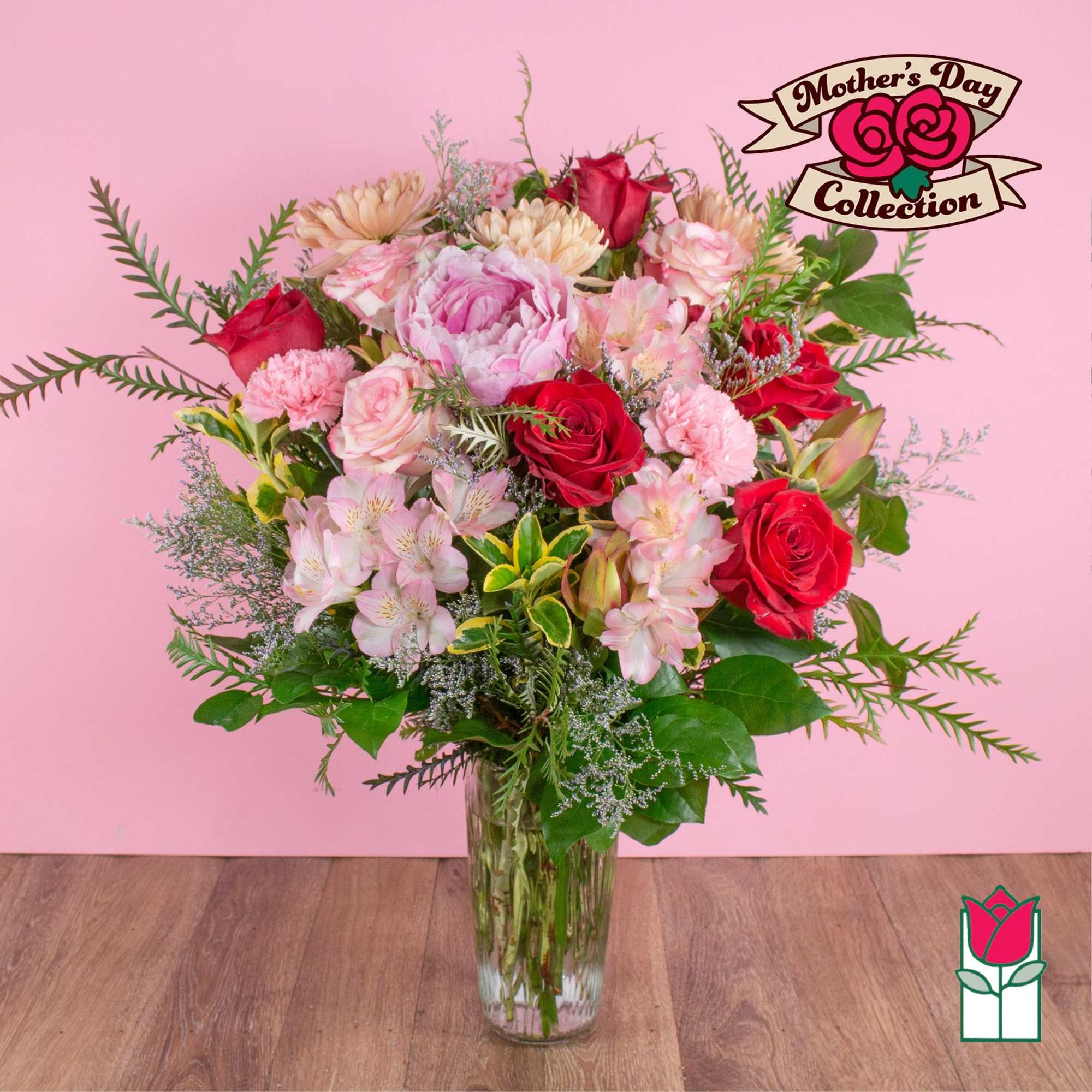 Tall mixed bouquet of pink and red flowers in a clear glass vase on a pink background