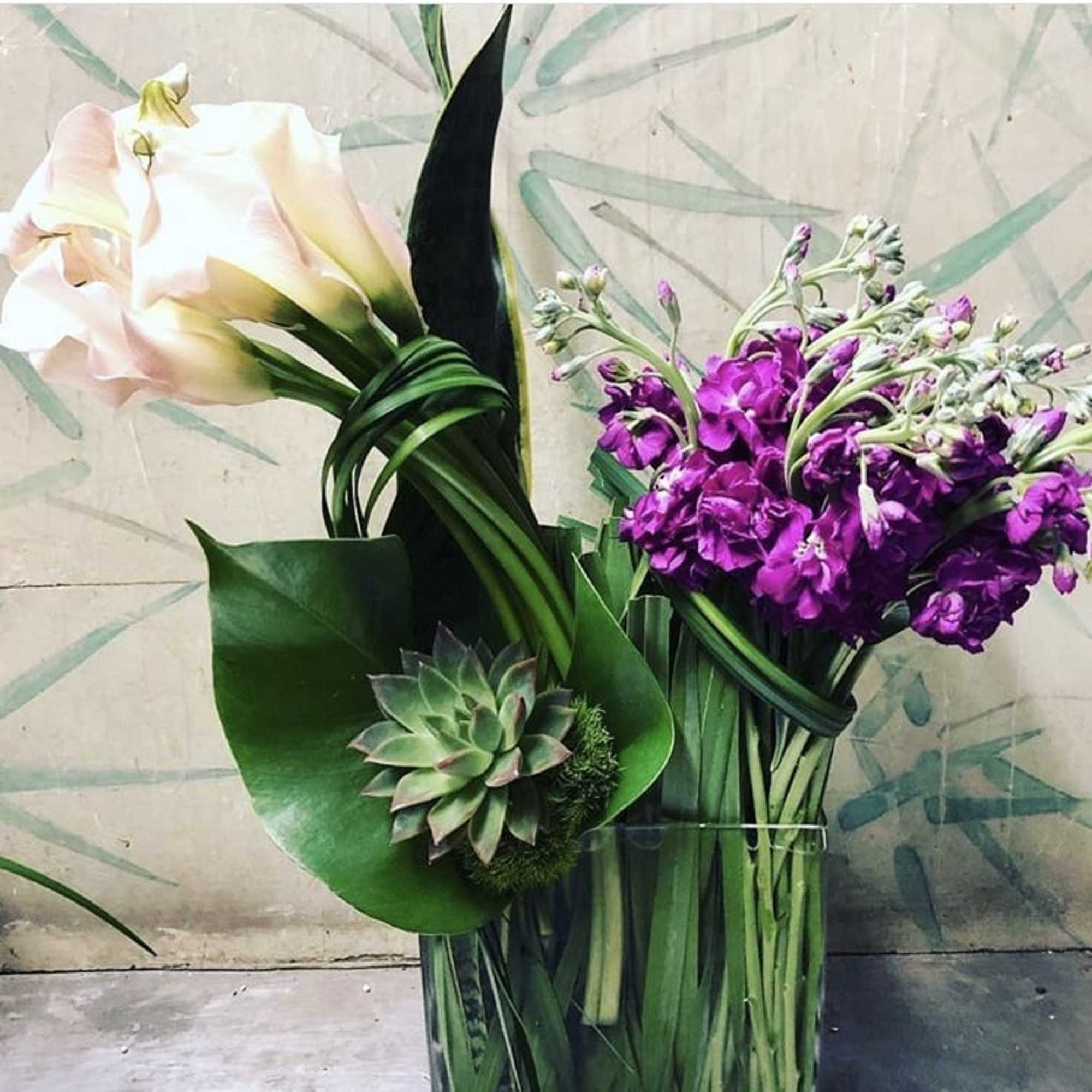 Bouquet with a pale calla lily, purple blooms, and a succulent in a glass vase