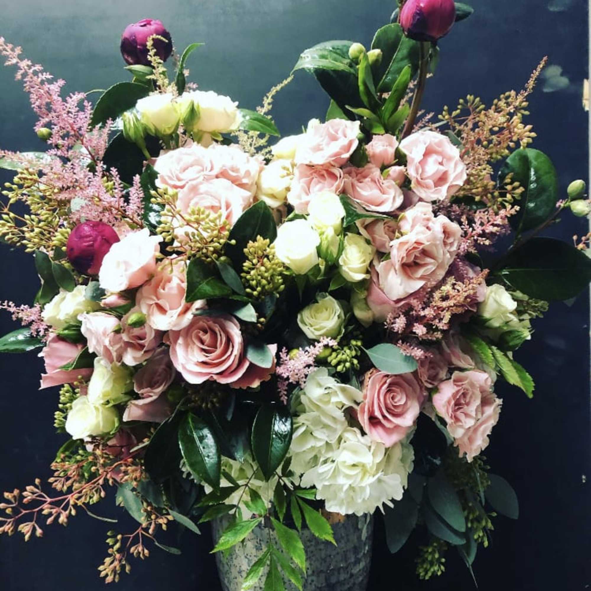 Pink and white roses arranged in a tall vase with dark foliage