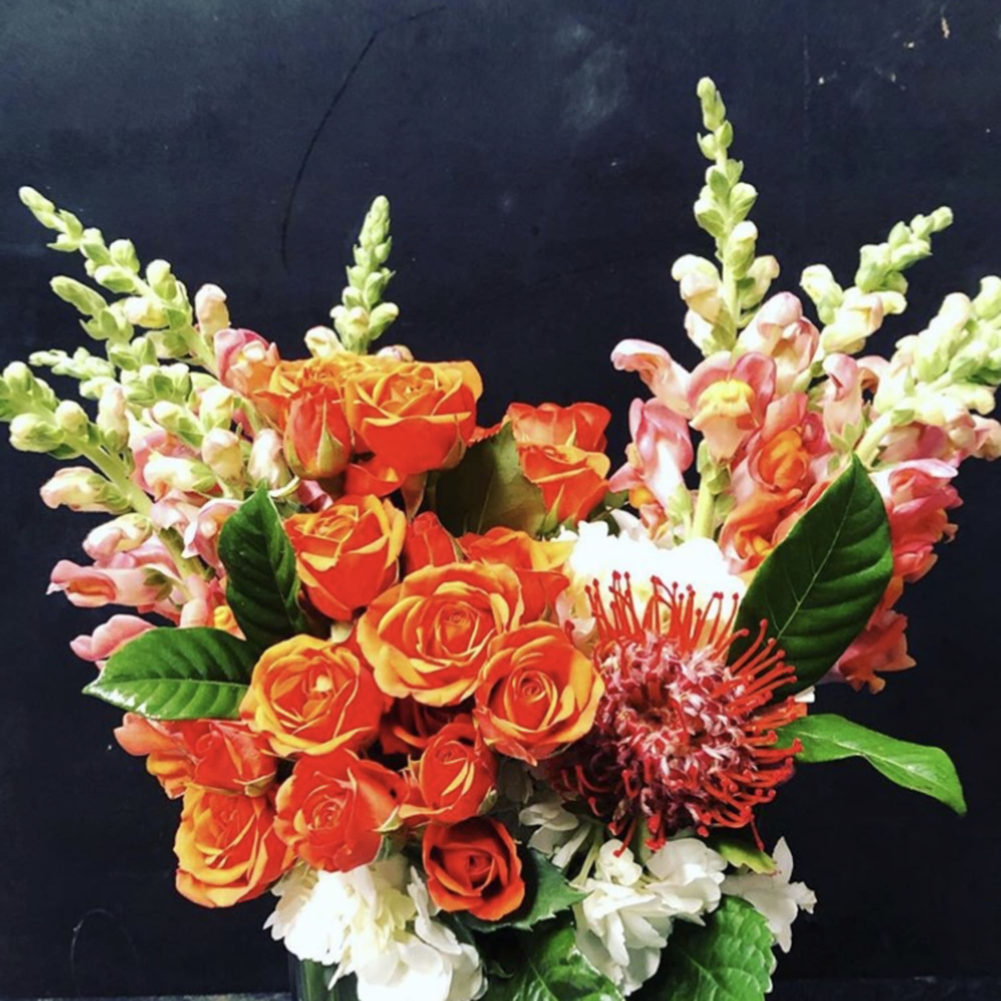 Orange roses with pink snapdragons in a glass vase