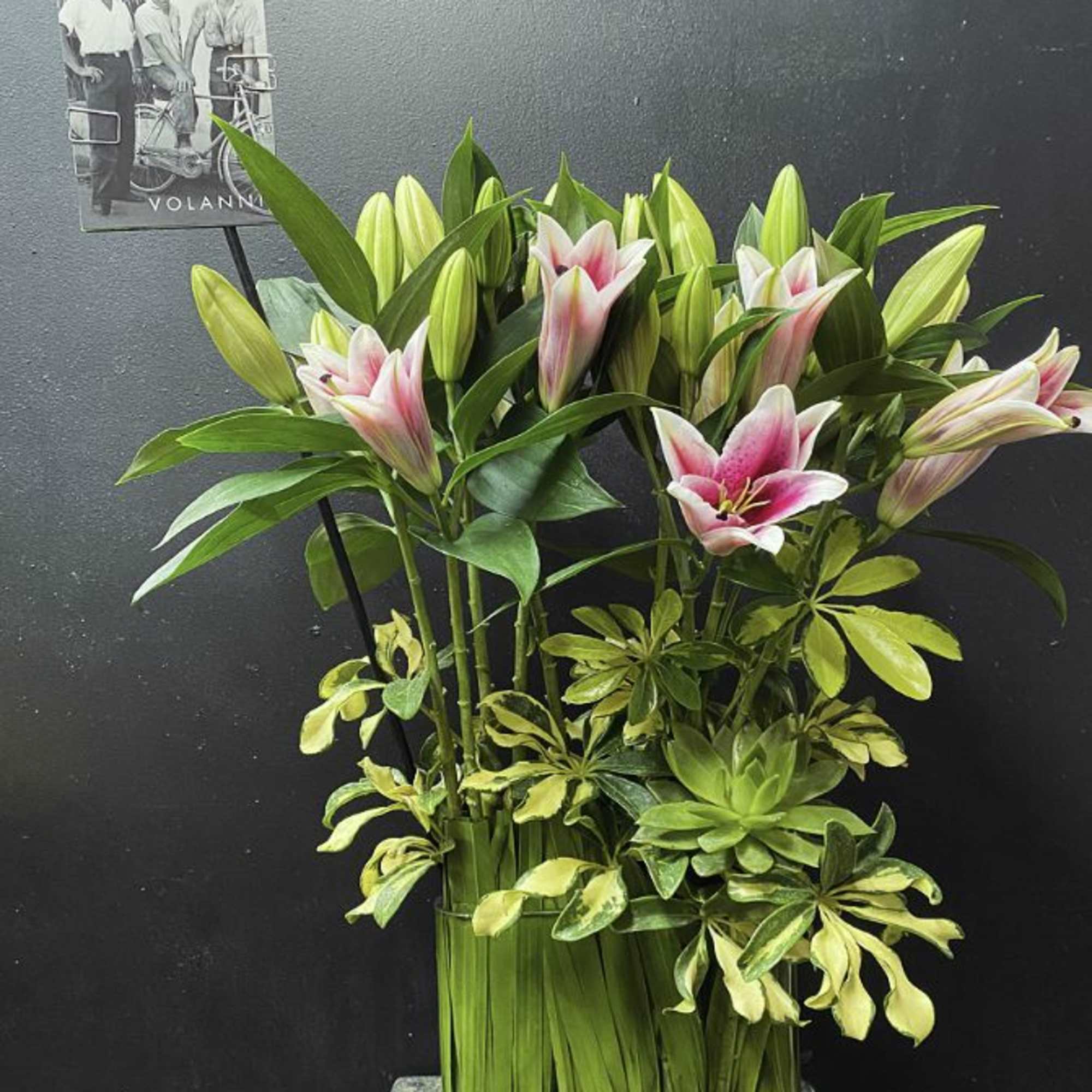 Pink and white lilies arranged with variegated greenery in a tall vase