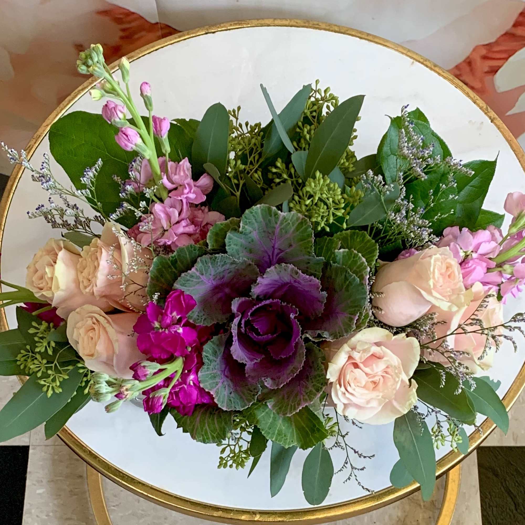 Pink and peach floral arrangement with purple center blooms in a round gold-rimmed vase