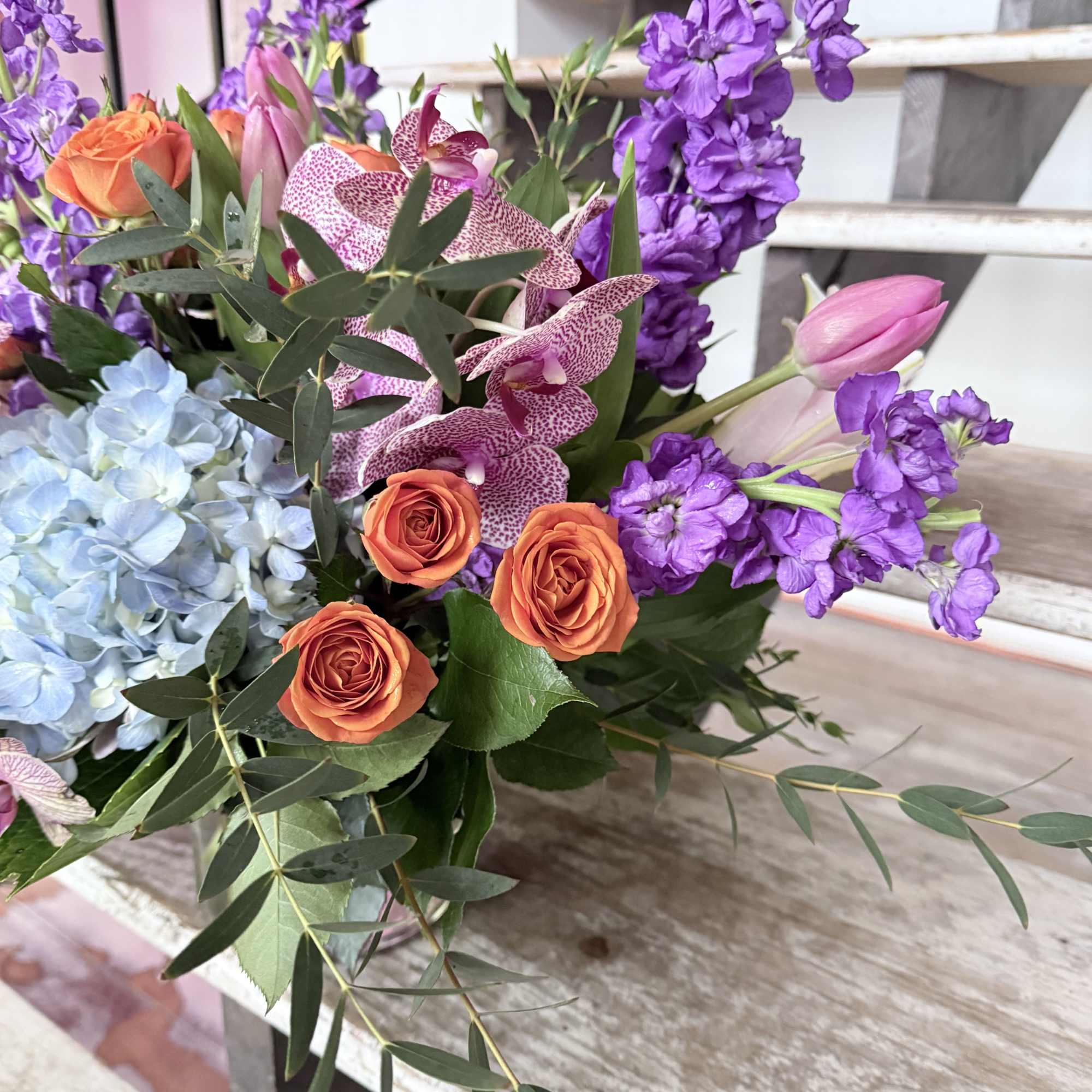 Bouquet of orange roses, purple orchids, and blue hydrangea