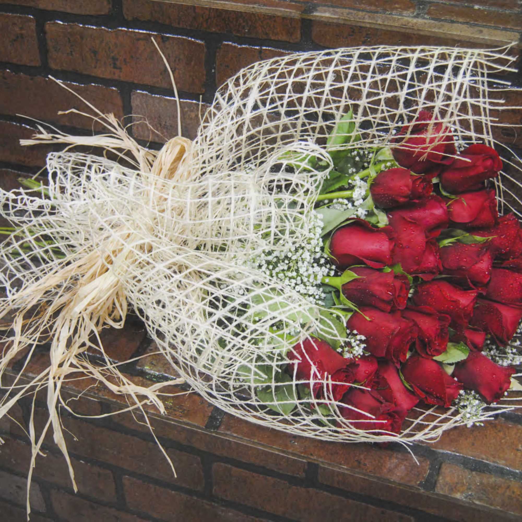 Bouquet of red roses wrapped in white mesh with straw accents