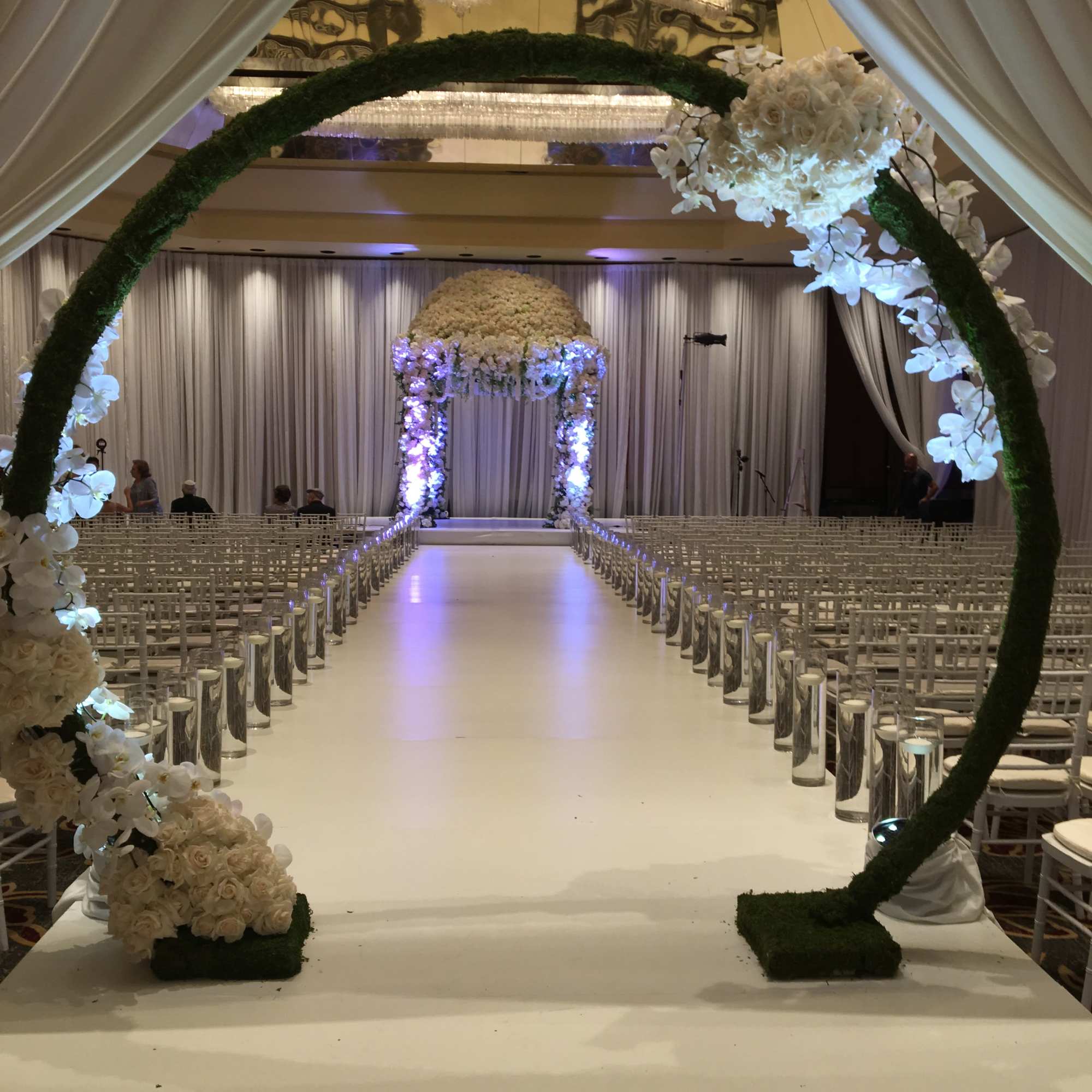 White floral wedding arch framing an aisle in a decorated ballroom