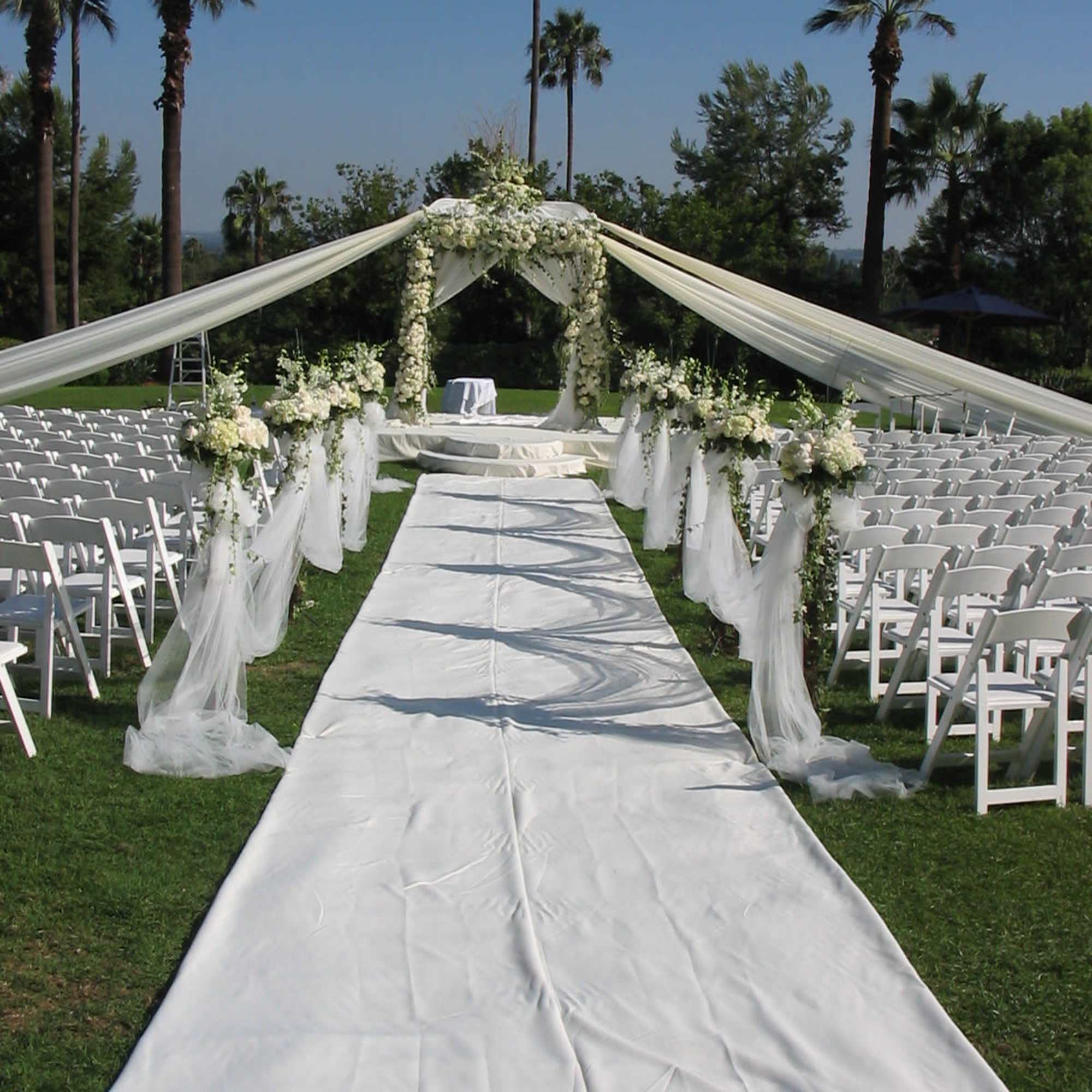 Outdoor wedding aisle with white draping and floral arch