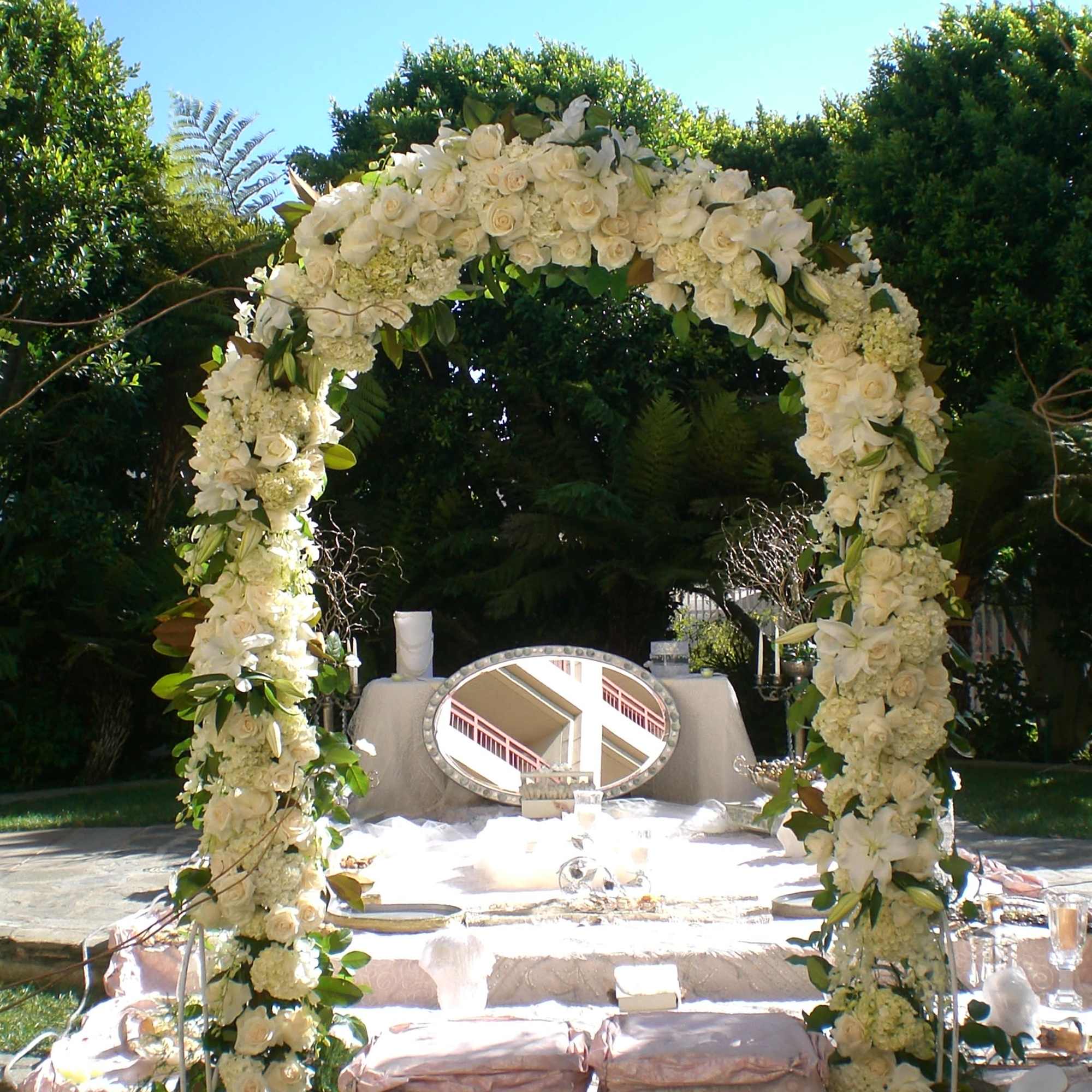 White floral arch over an outdoor ceremony table with candles and a mirror