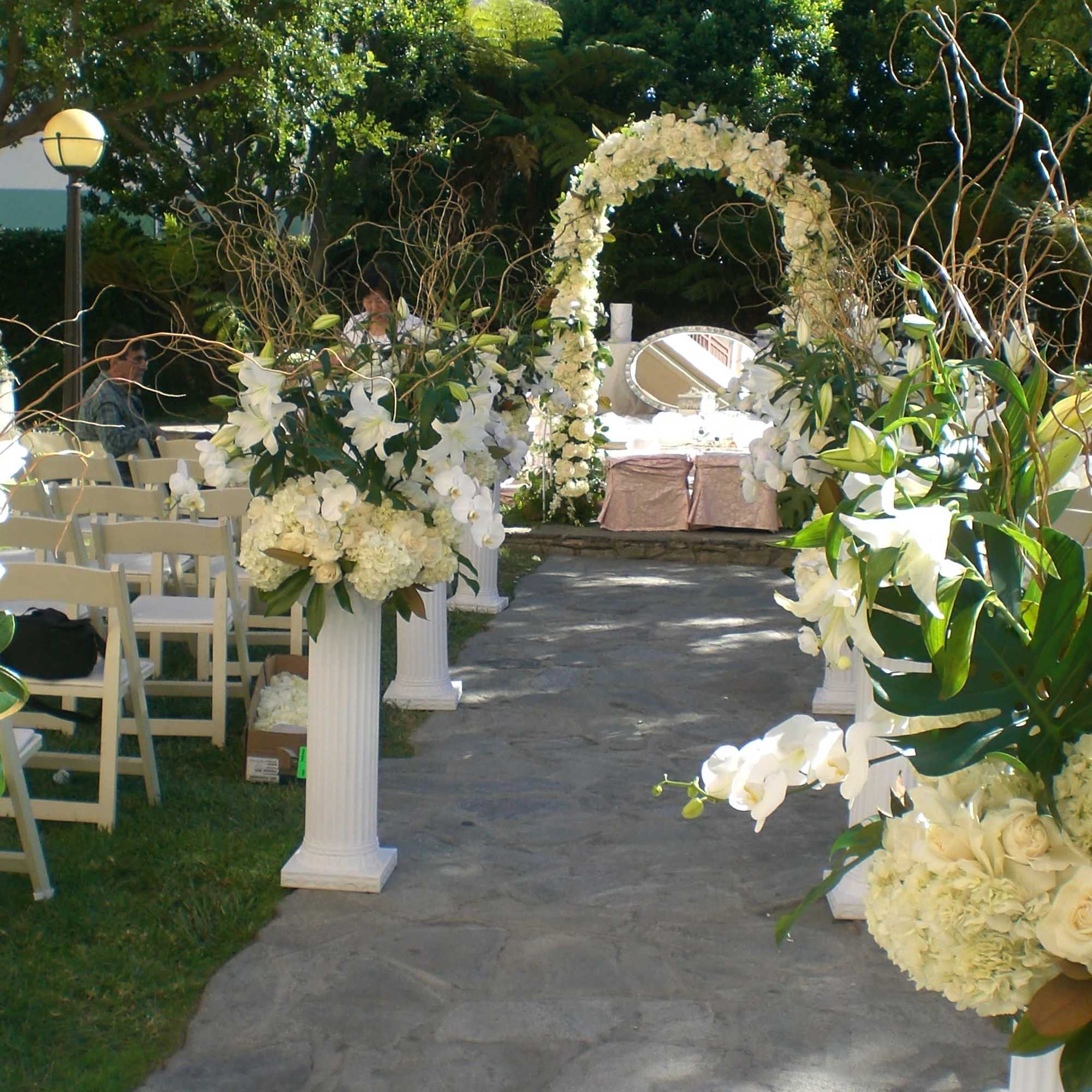 White floral wedding aisle with arch and pedestal arrangements