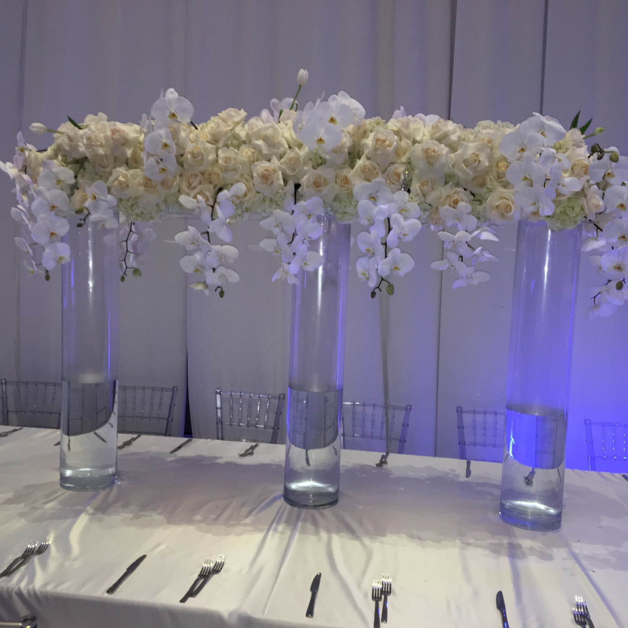 White floral centerpiece in tall glass vases on a banquet table