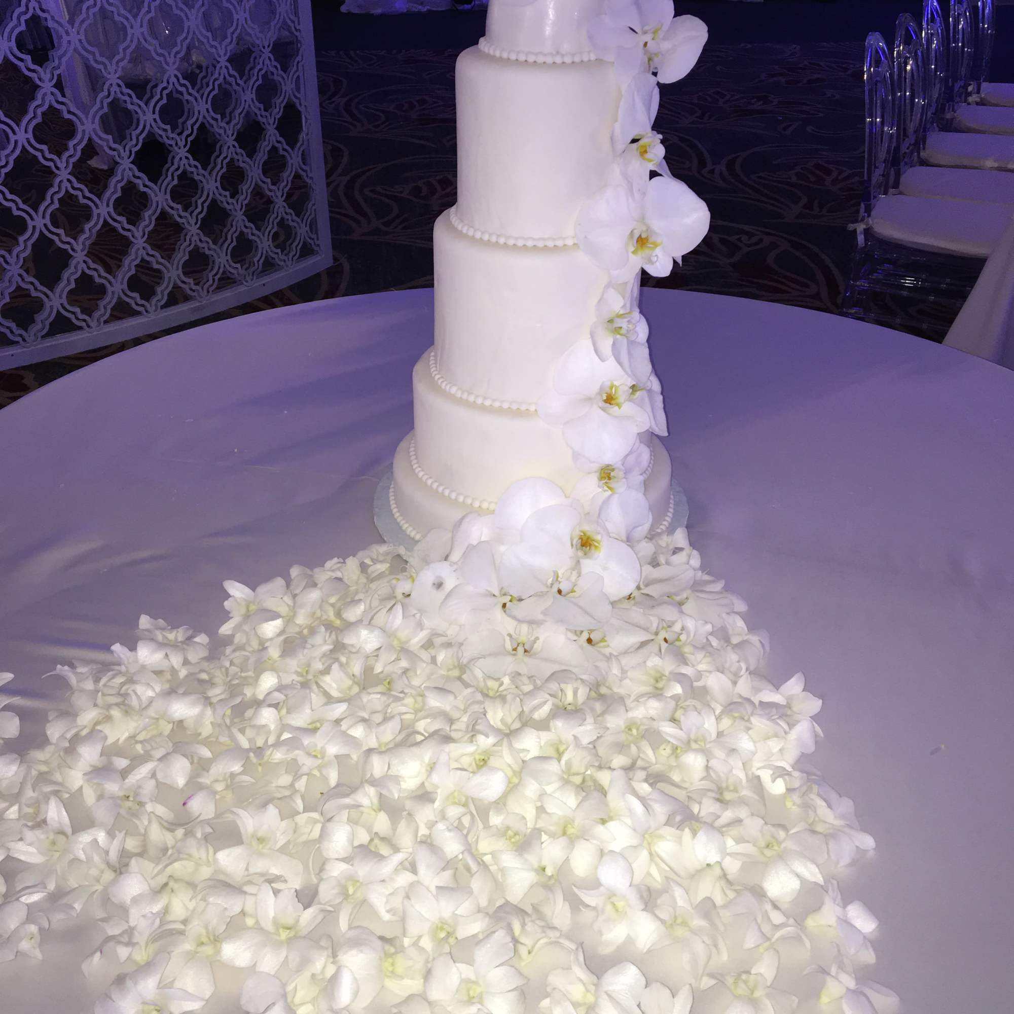 White tiered wedding cake with cascading orchids on a round table
