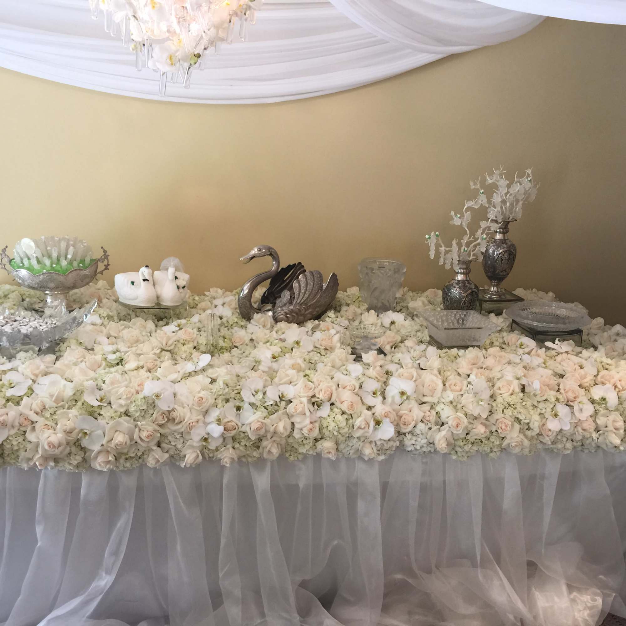 Large table covered in white and blush roses with silver decor pieces