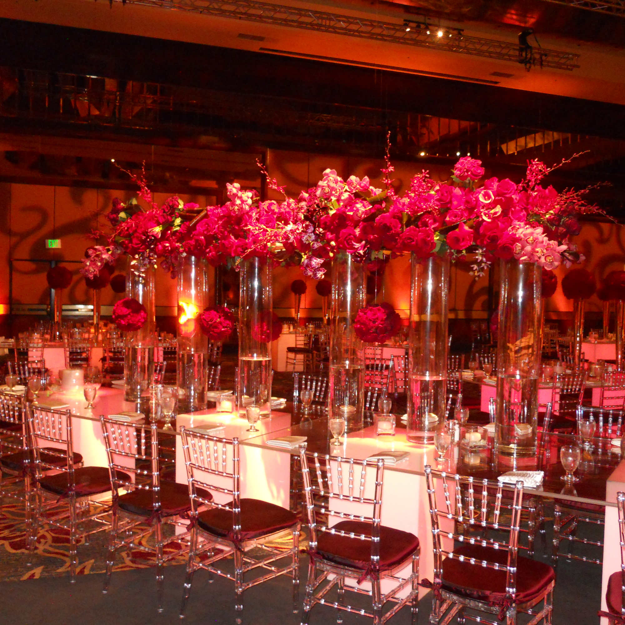 Tall pink floral centerpieces in clear glass cylinders on banquet tables