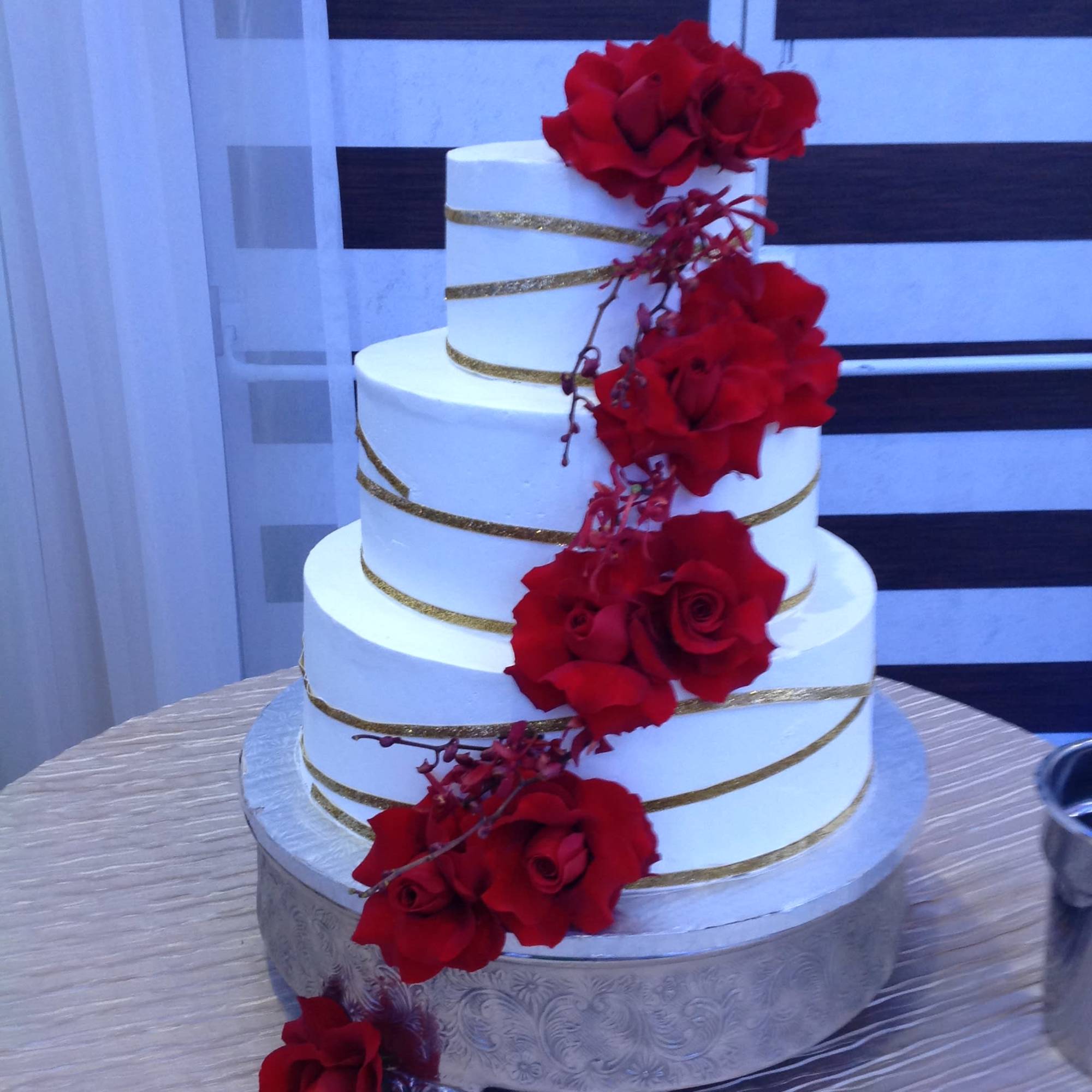 Three-tier white cake with red roses and gold ribbon bands