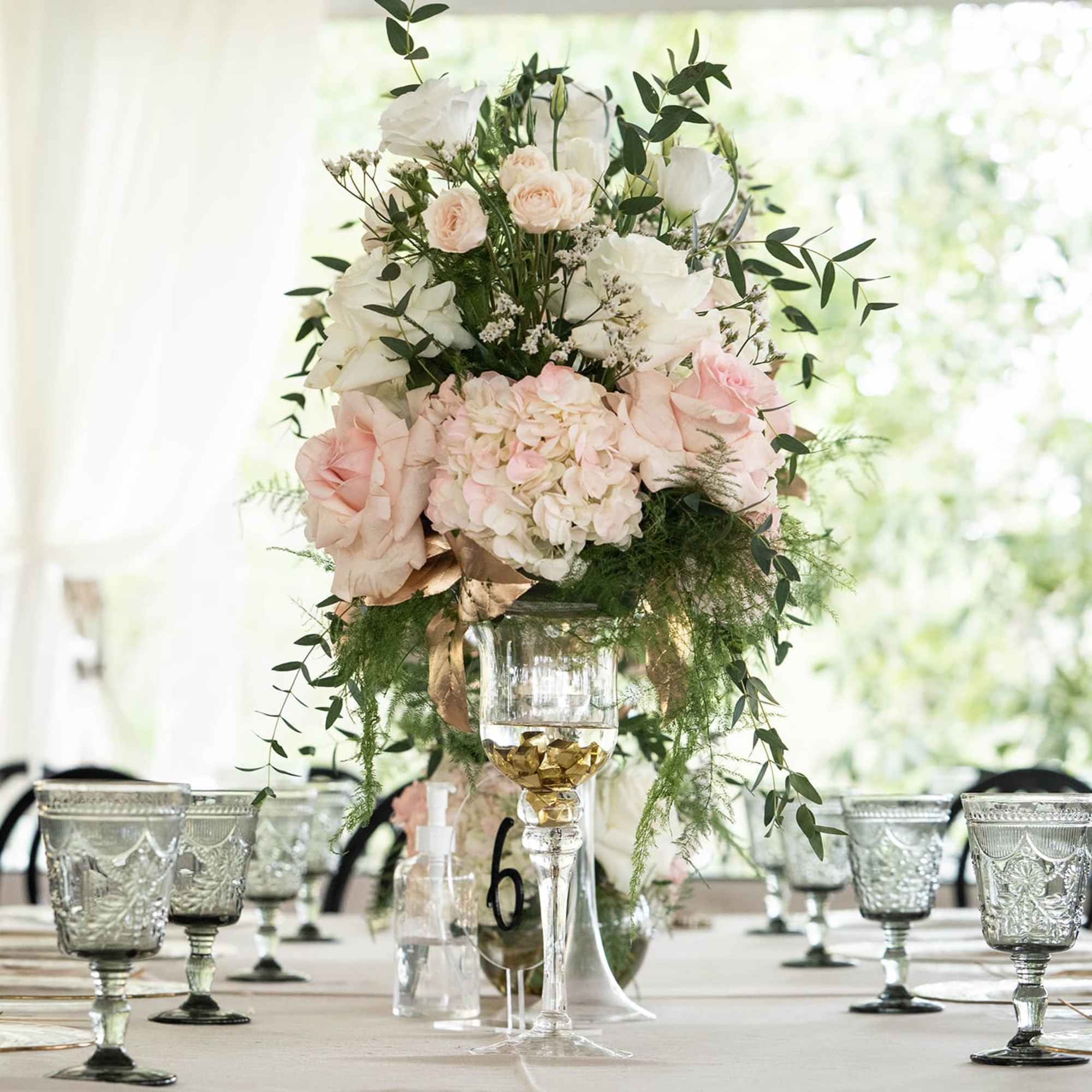 Tall floral centerpiece with pale pink and white roses in a glass vase
