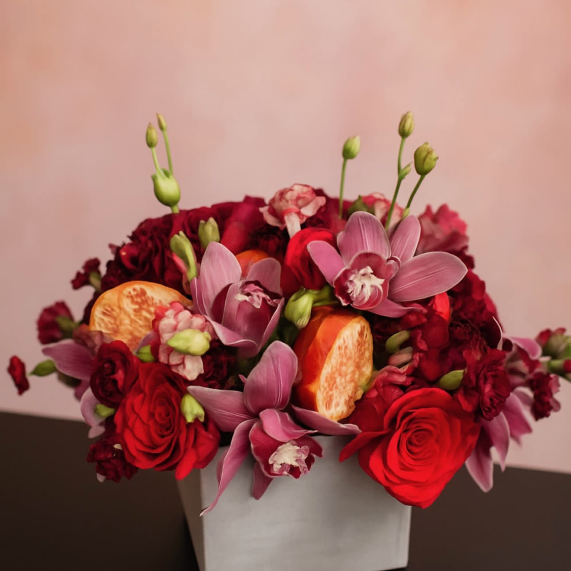Red and pink floral arrangement in a white square vase
