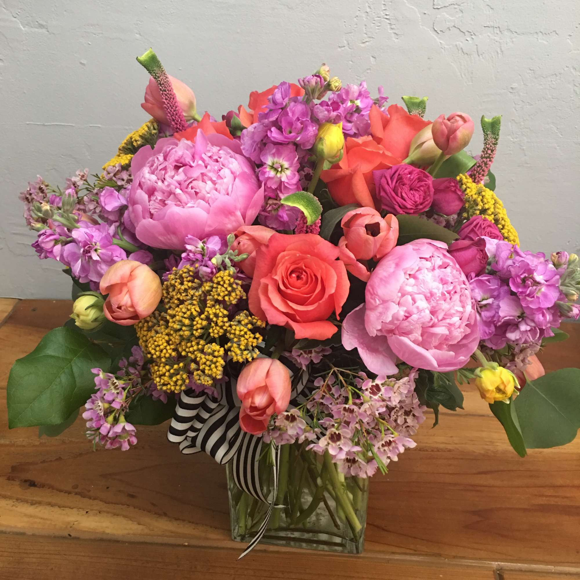Mixed bouquet of pink and coral flowers in a glass vase with striped ribbon