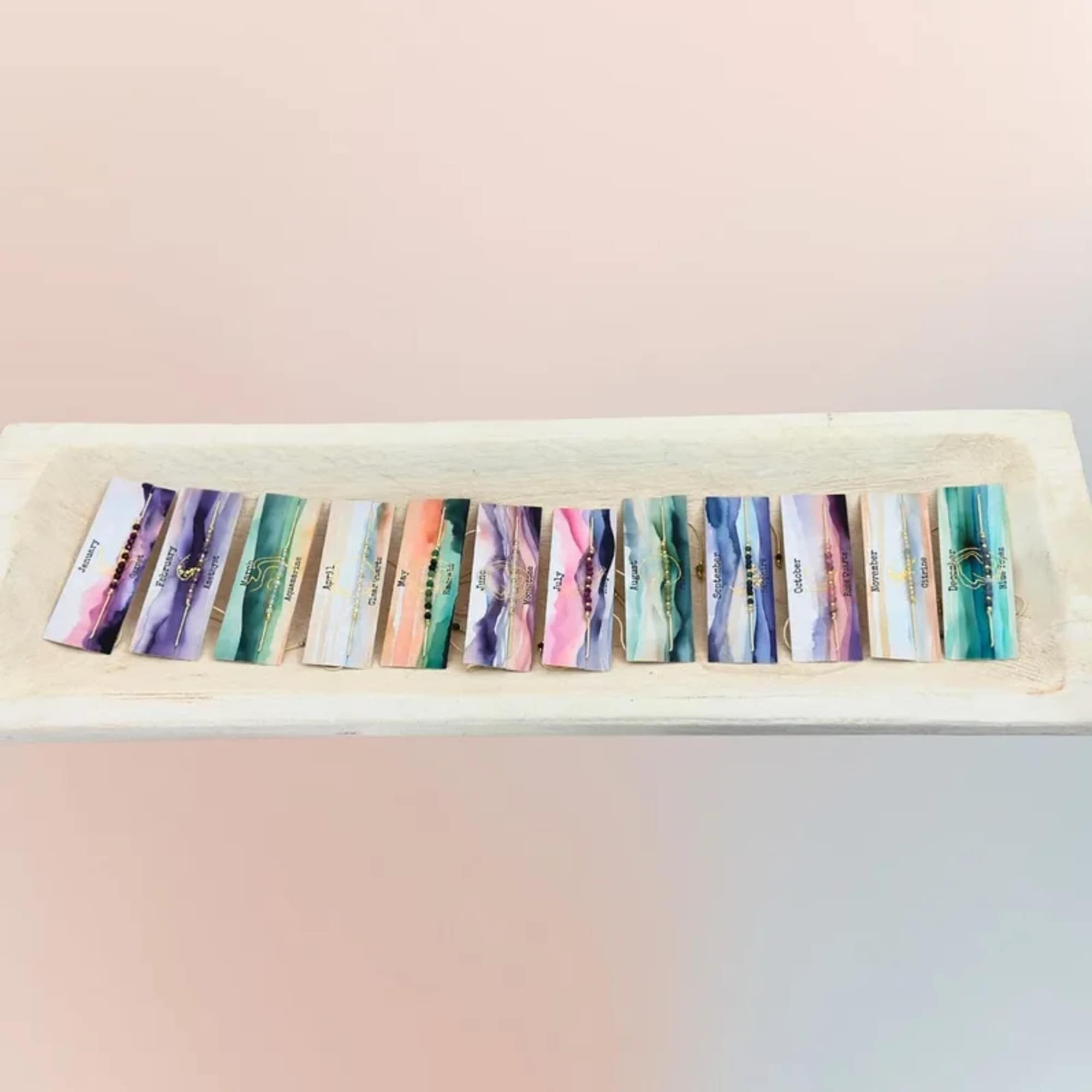 A tray holds a row of colorful month-labeled cards with small gold charms.