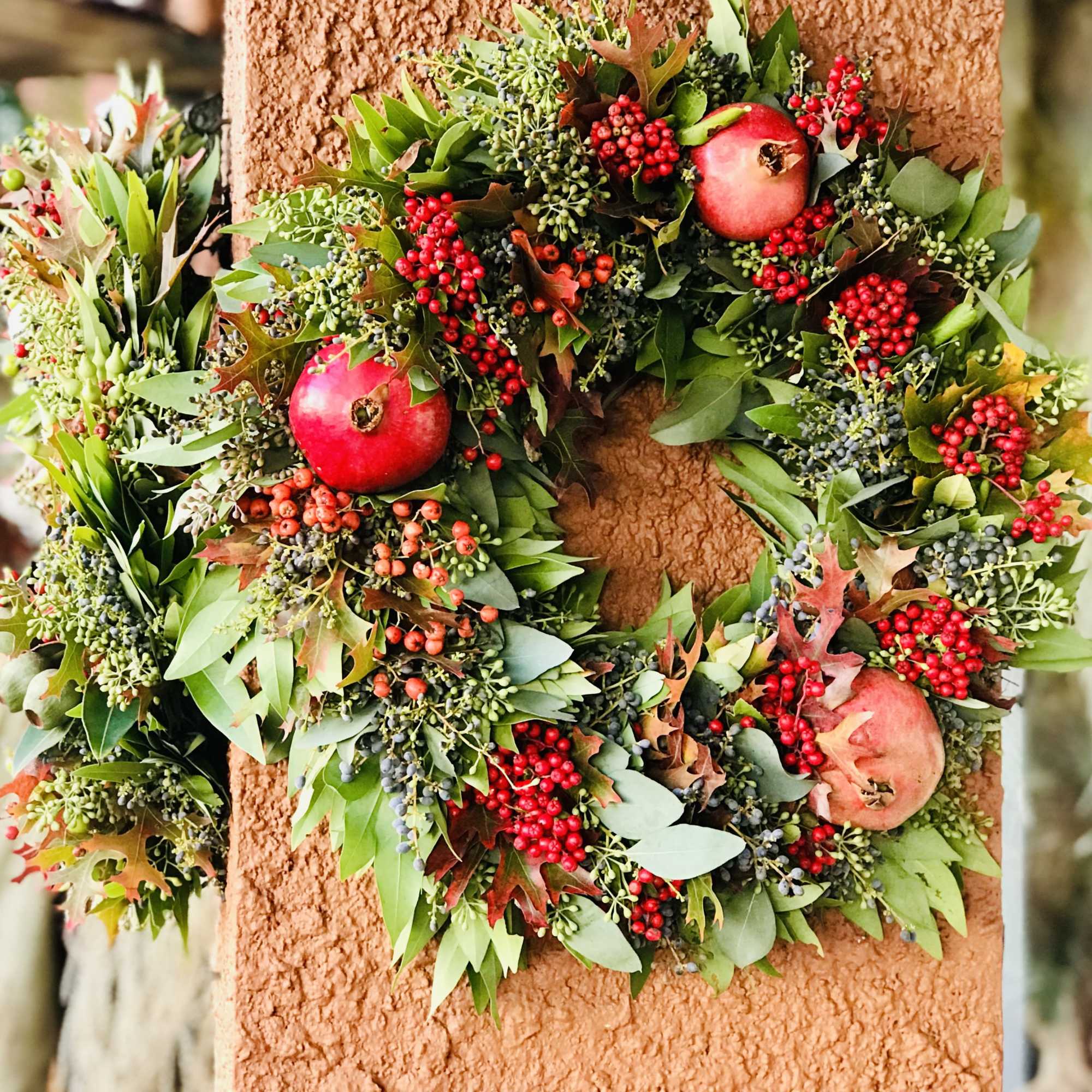 Autumn wreath with red berries and pomegranates on a textured wall