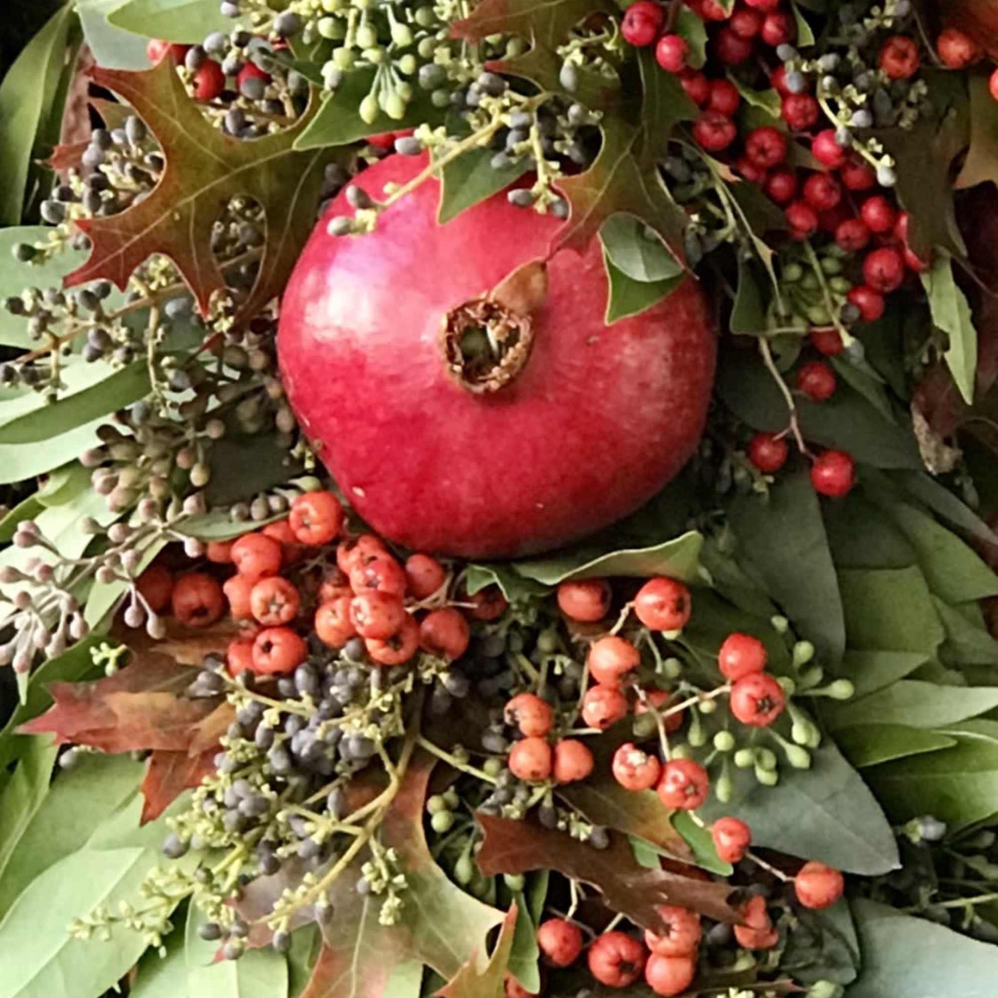 Pomegranate surrounded by red berries and mixed greenery