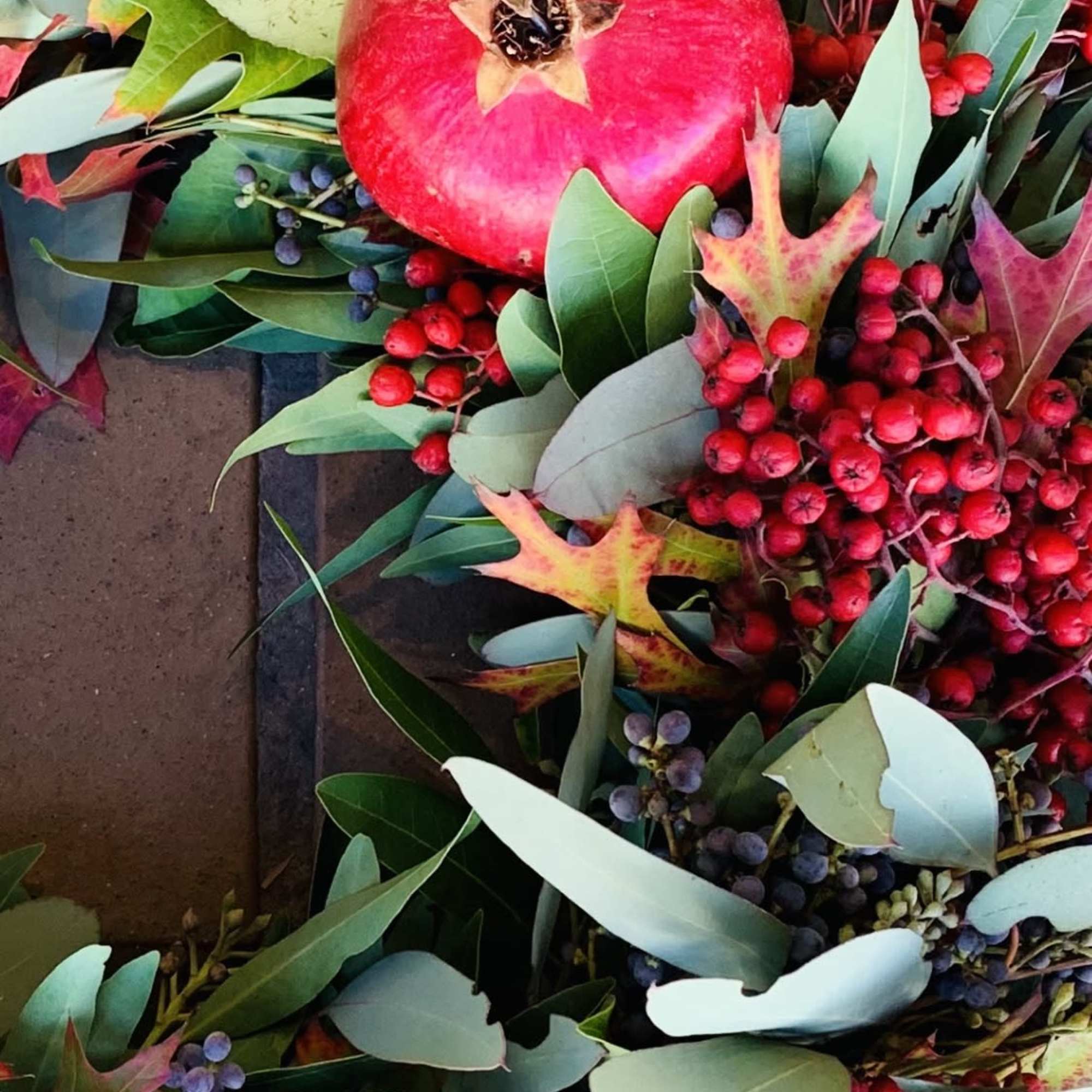 Pomegranate wreath with red berries and mixed green leaves