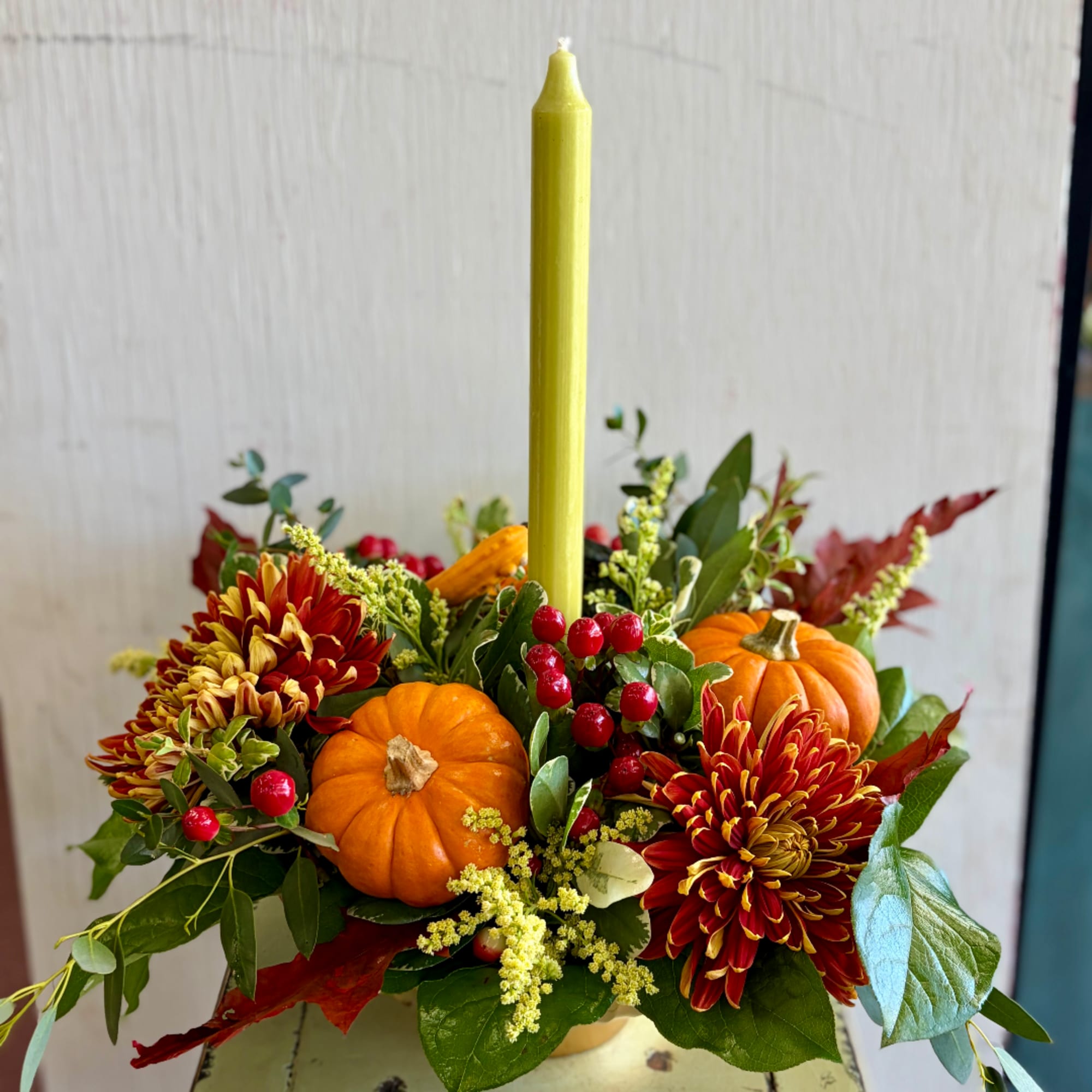 Autumn centerpiece with orange pumpkins, red-yellow mums, and a tall candle