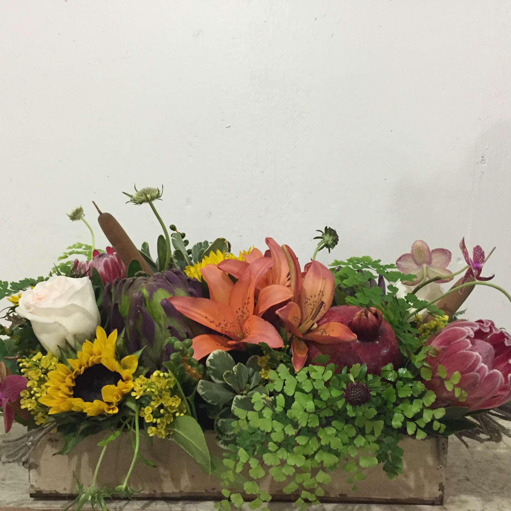 Mixed floral arrangement with lilies, sunflowers, roses, and protea in a low container