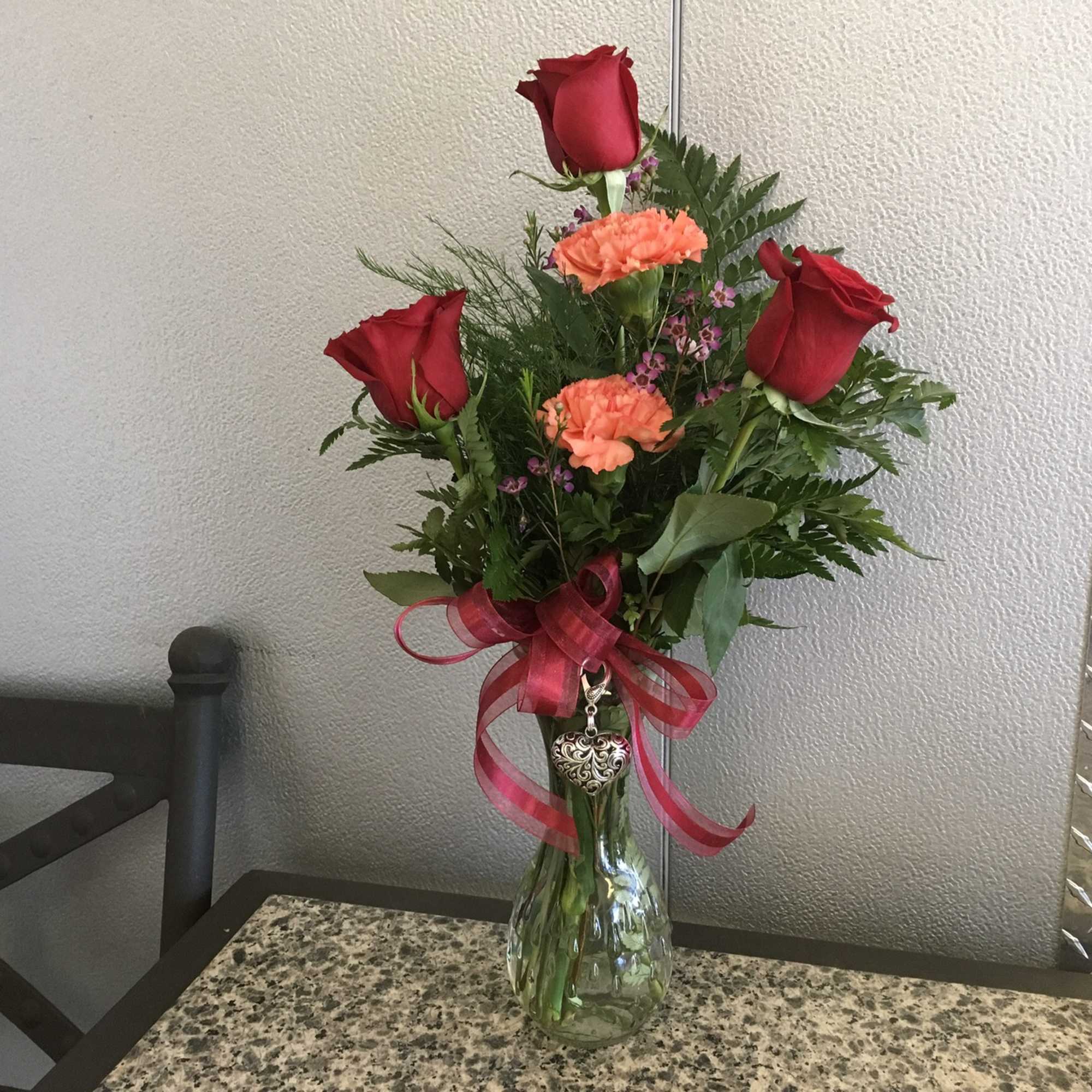 Red roses and orange carnations in a glass vase with a pink ribbon