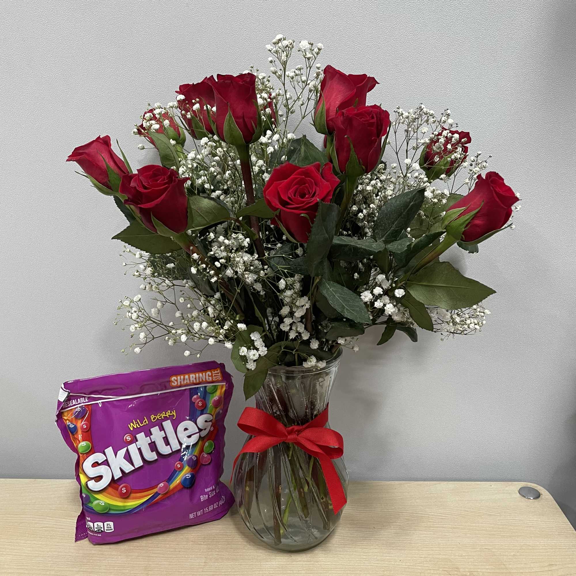 Red roses in a glass vase with a bag of Skittles candy