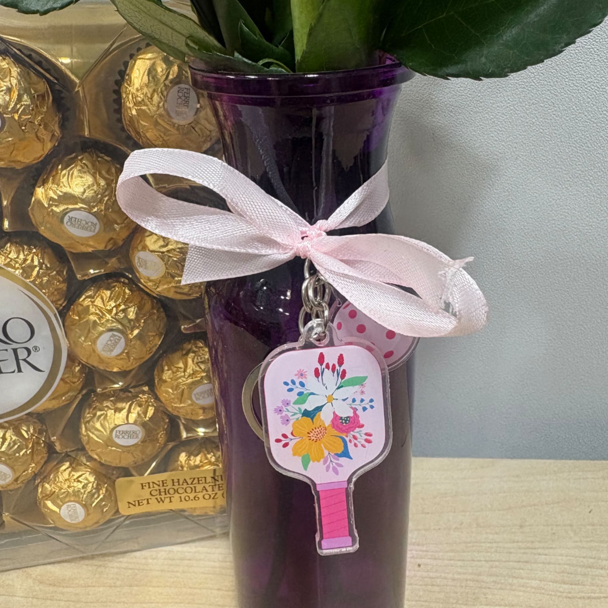 Purple vase with a pink ribbon and floral keychain beside a box of chocolates