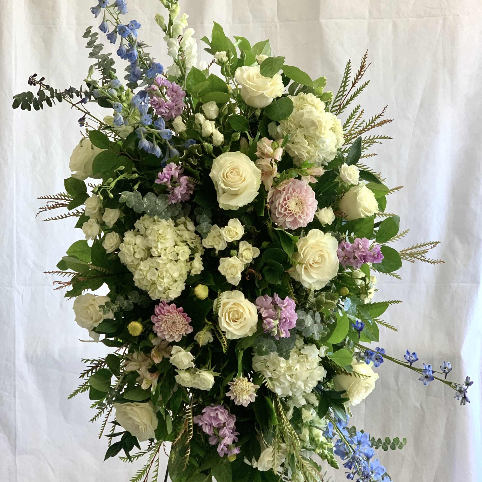 Large standing floral spray with white roses, hydrangeas, and blue delphinium
