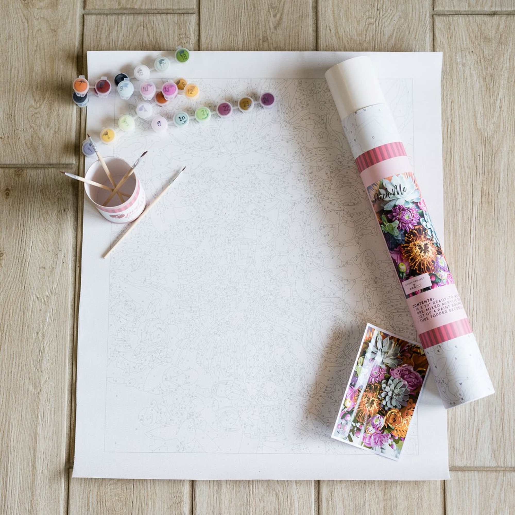 Paint-by-number floral print with paint pots and brushes on a wooden floor