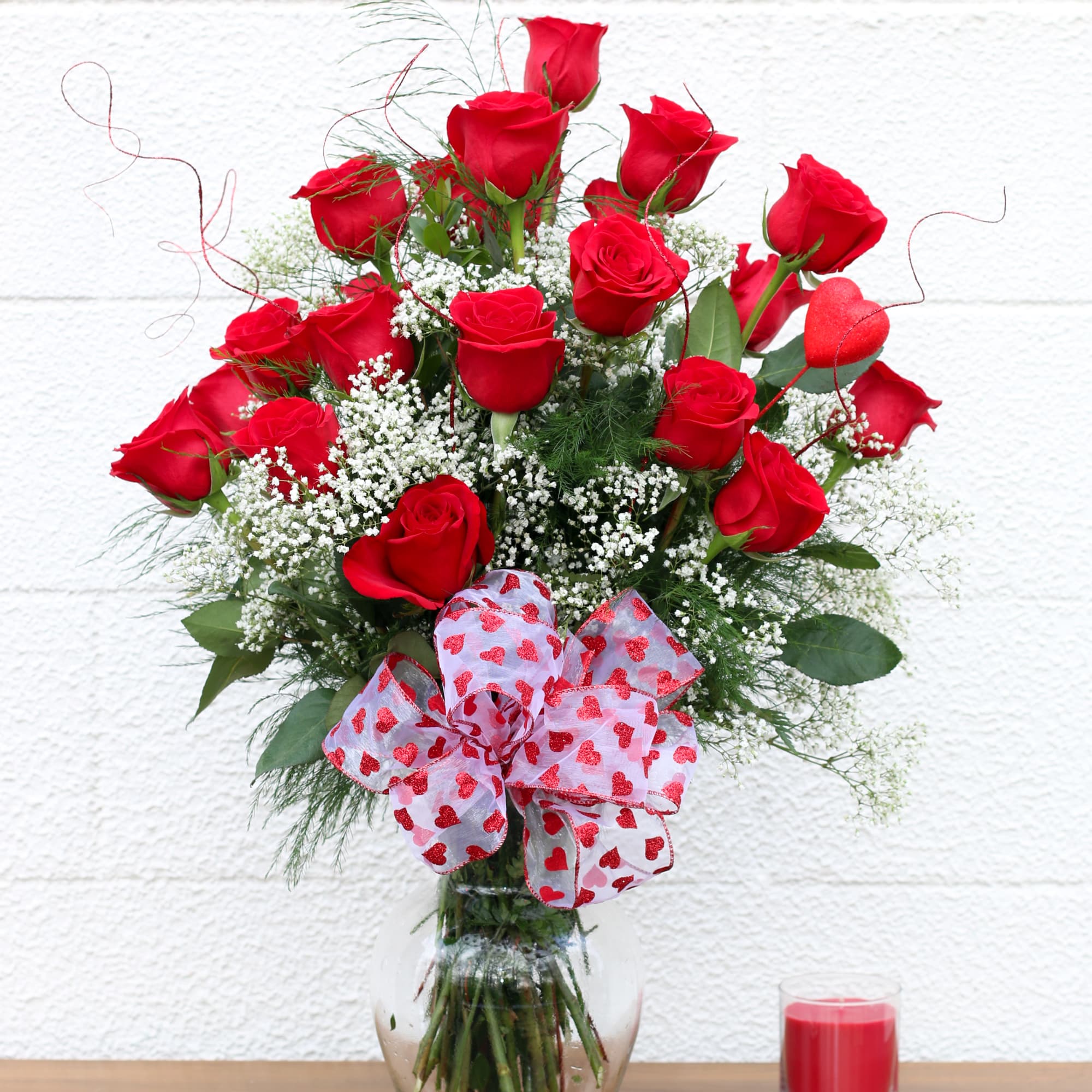 Red roses in a glass vase with a heart-patterned bow