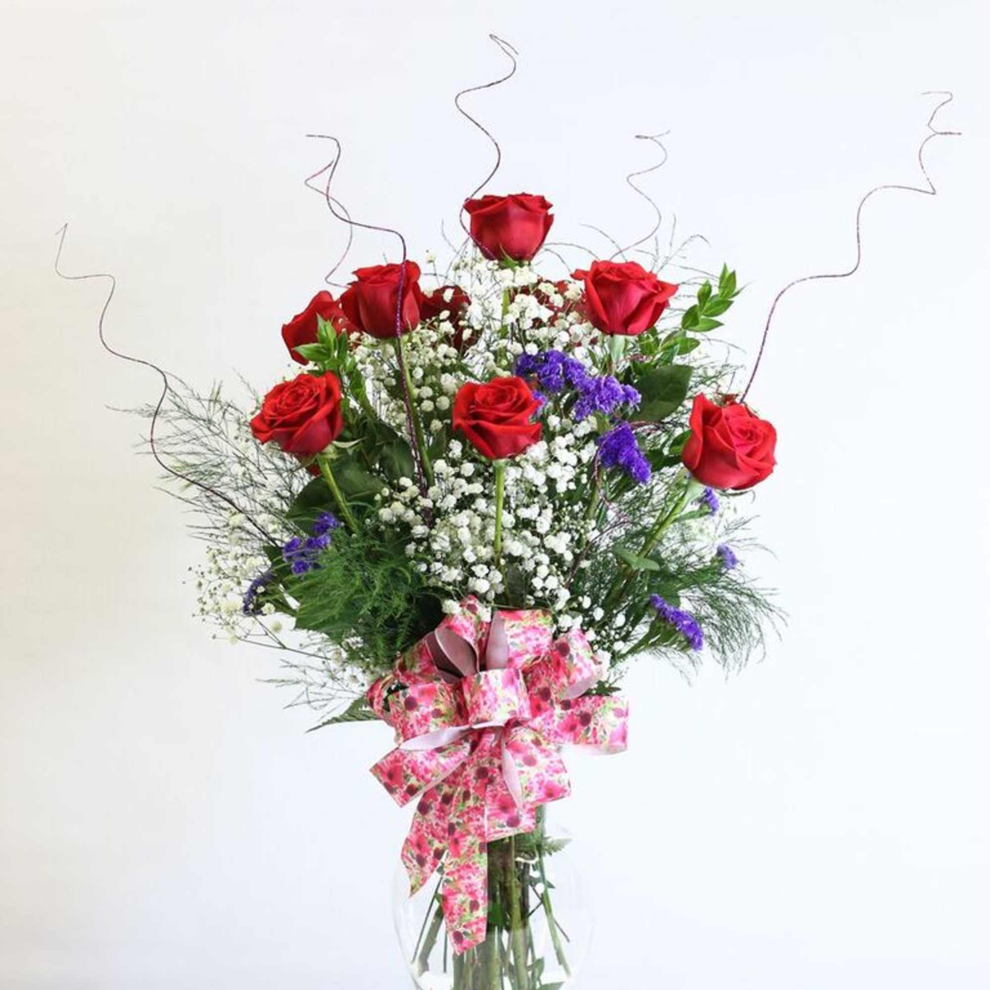 Red roses in a clear vase with baby's breath and a pink ribbon bow